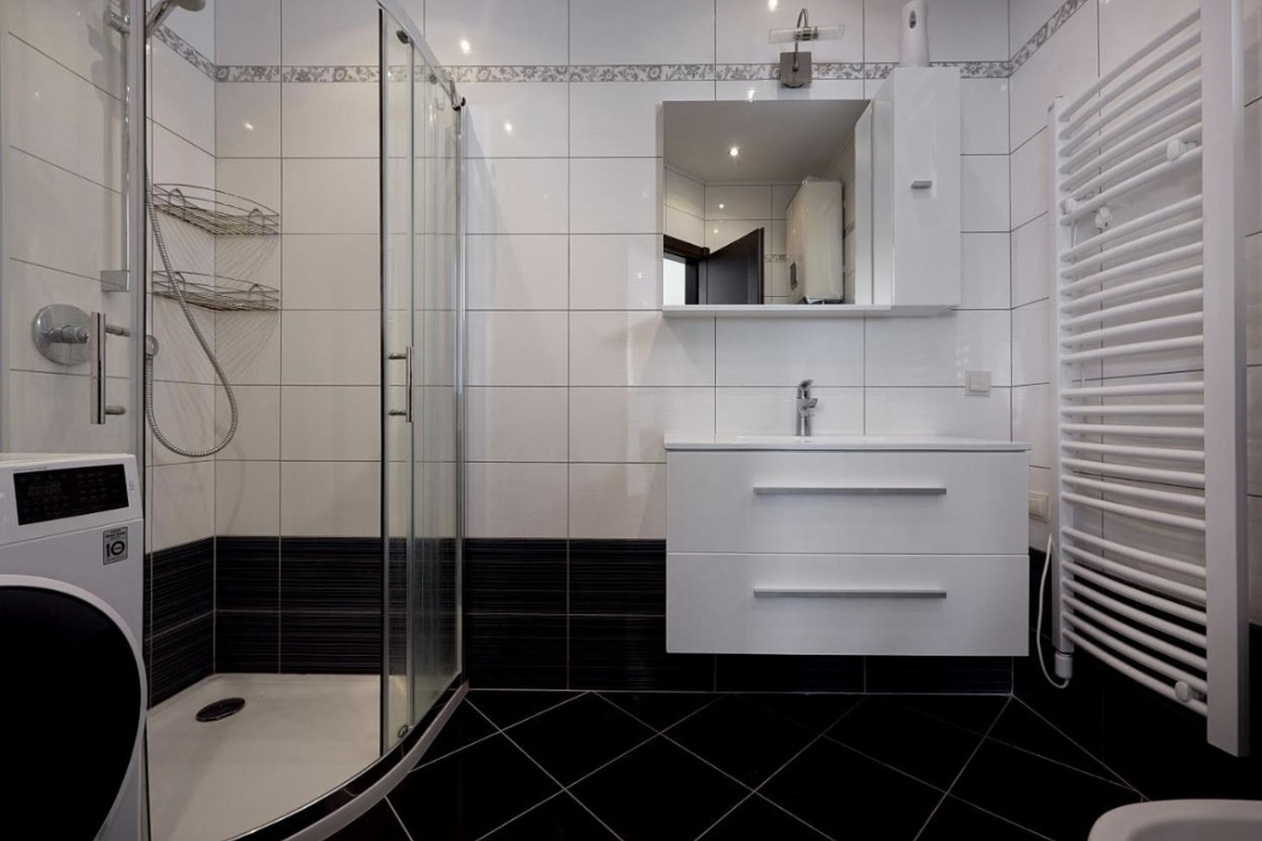 Modern bathroom with a shower cabin in an apartment in Bečići, Montenegro: white tiles, vanity unit, and towel warmer.