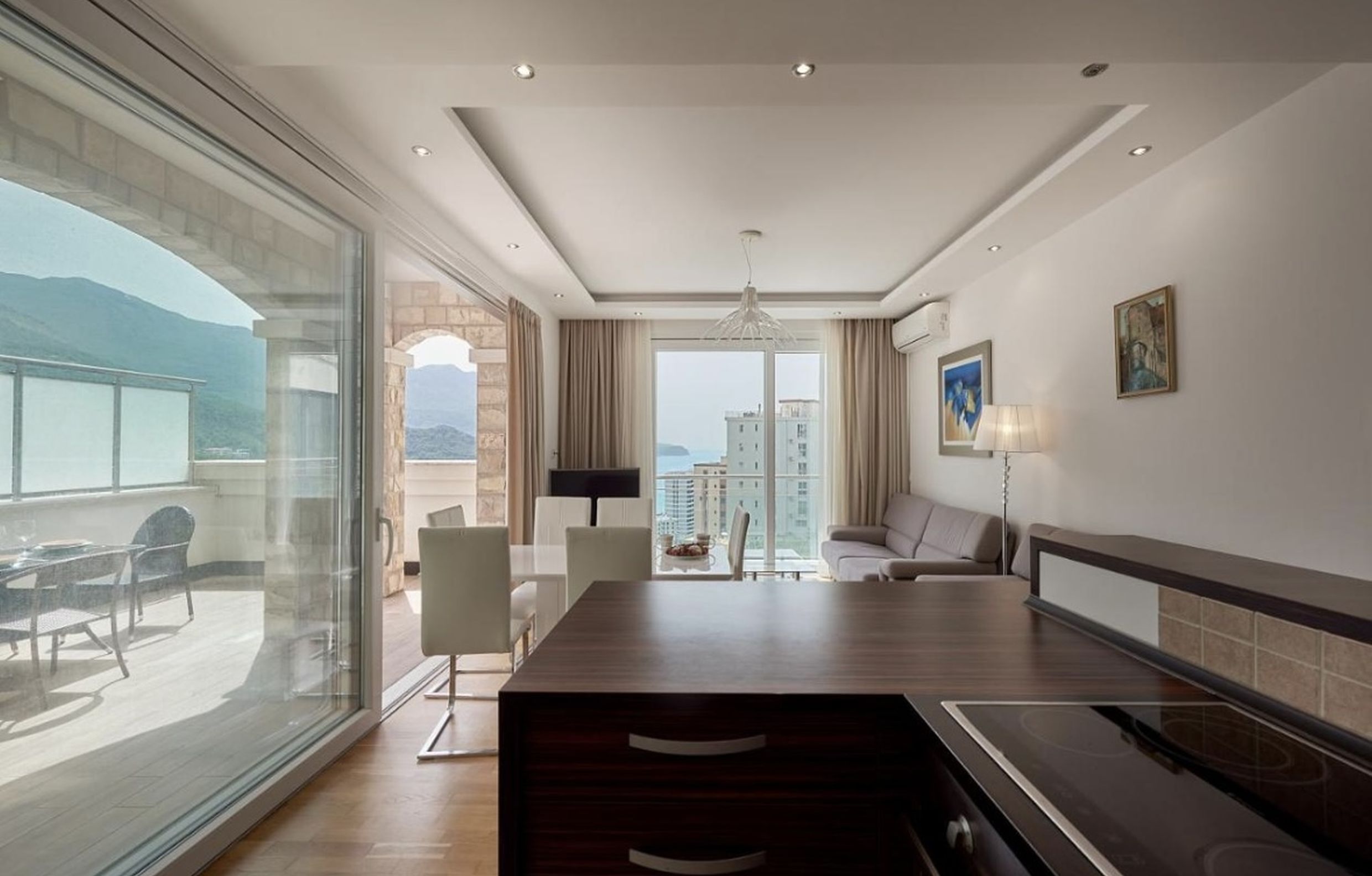 Living room with kitchen in an apartment in Bečići, Montenegro: panoramic windows, sea view, and terrace access.