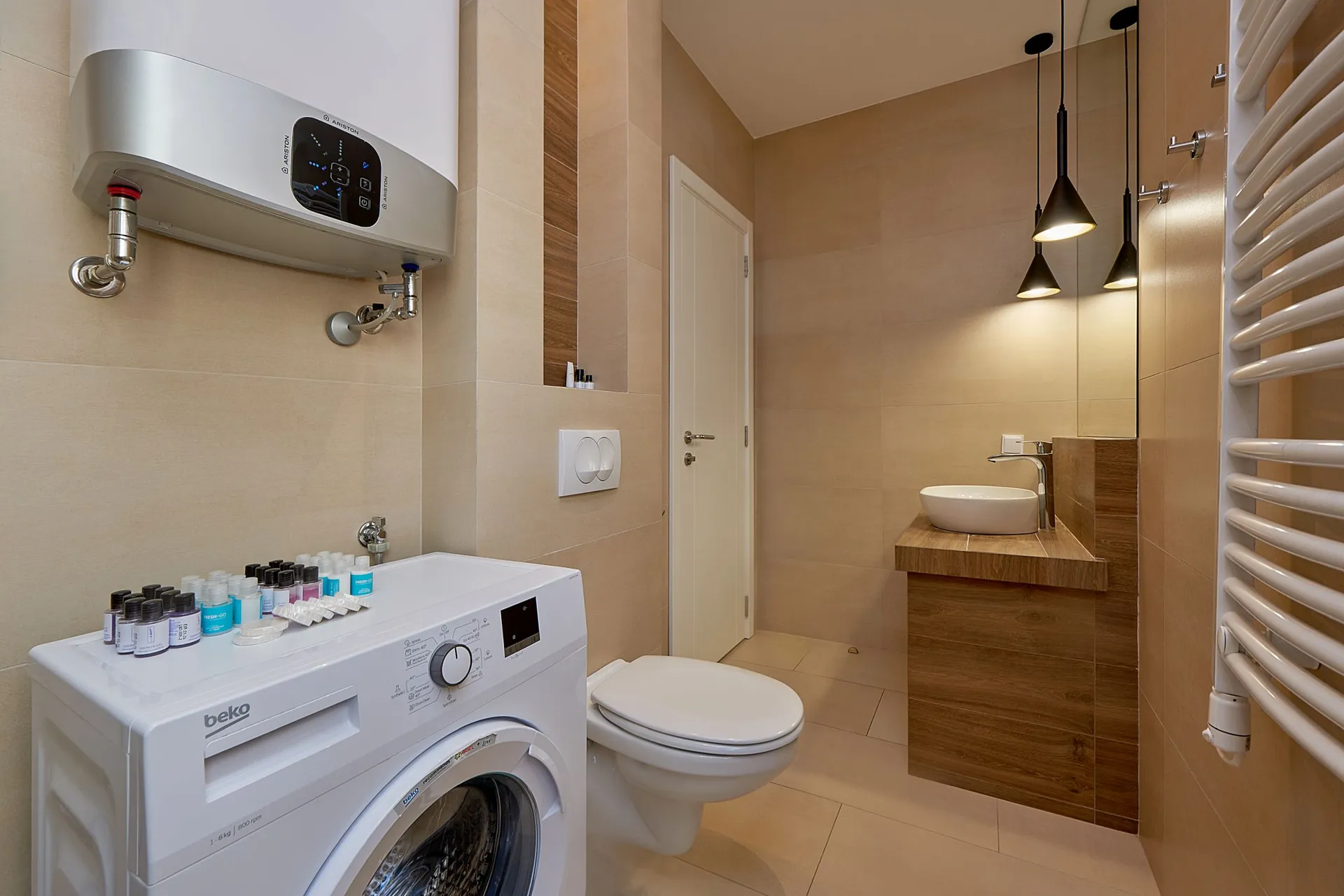Modern bathroom featuring a washing machine, wall-mounted toilet, and vessel sink on a wooden vanity unit.