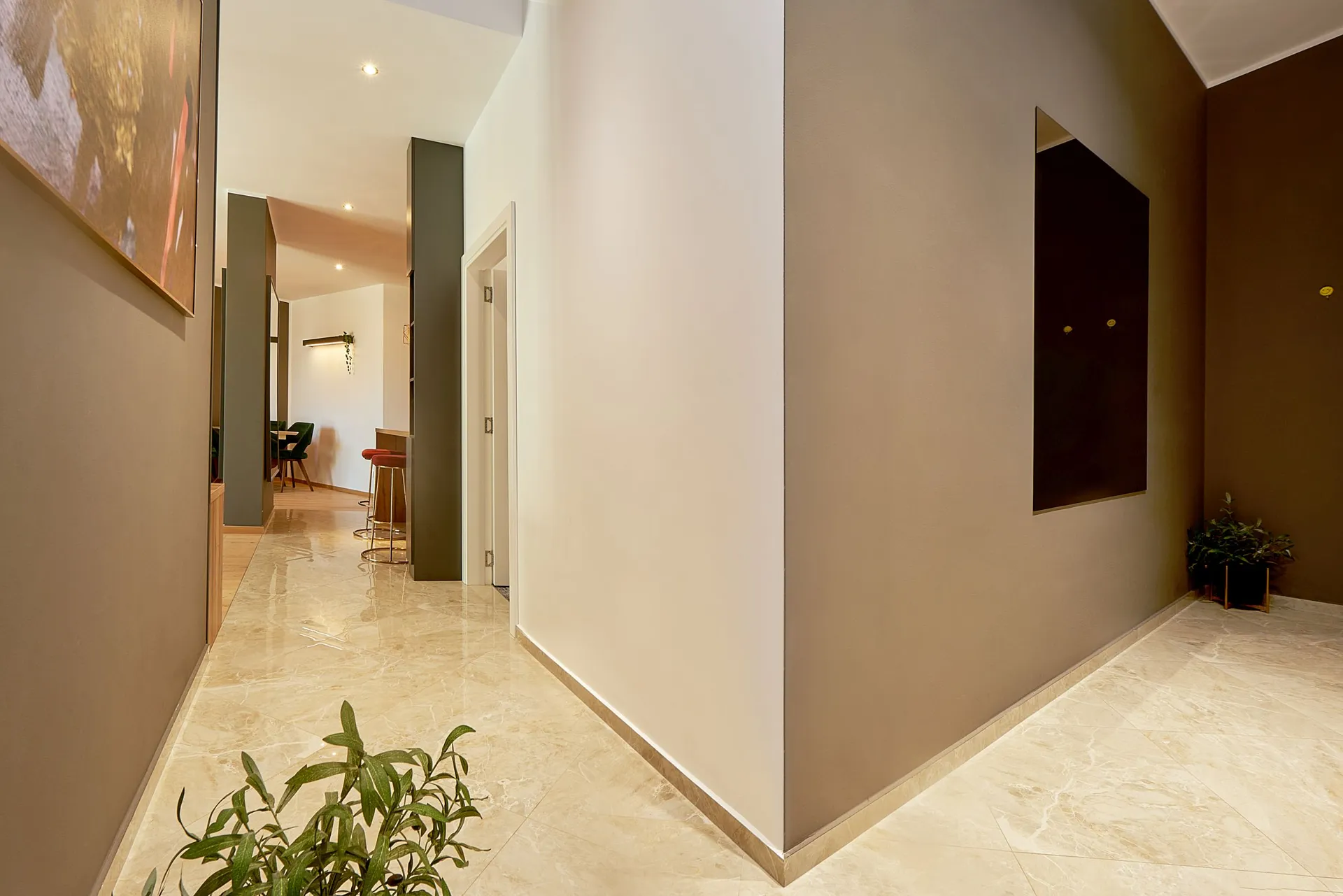 Modern hallway with marble flooring and beige walls featuring abstract art. In the background, a seating area with bar stools is visible.