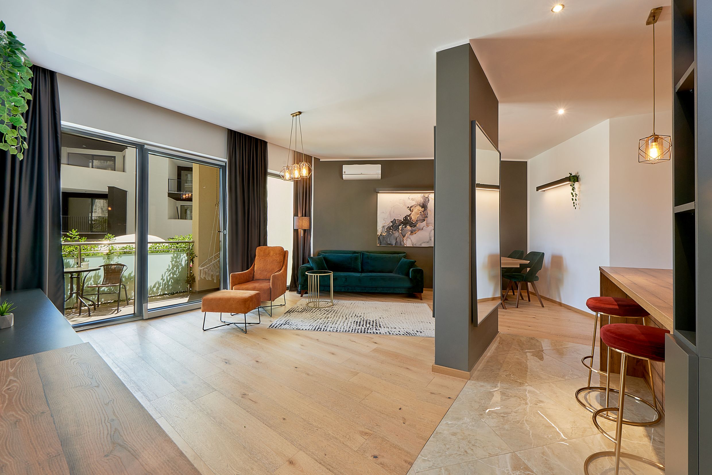Modern living room in Bečići apartments, Montenegro: emerald sofa, terracotta armchair, and terrace access.