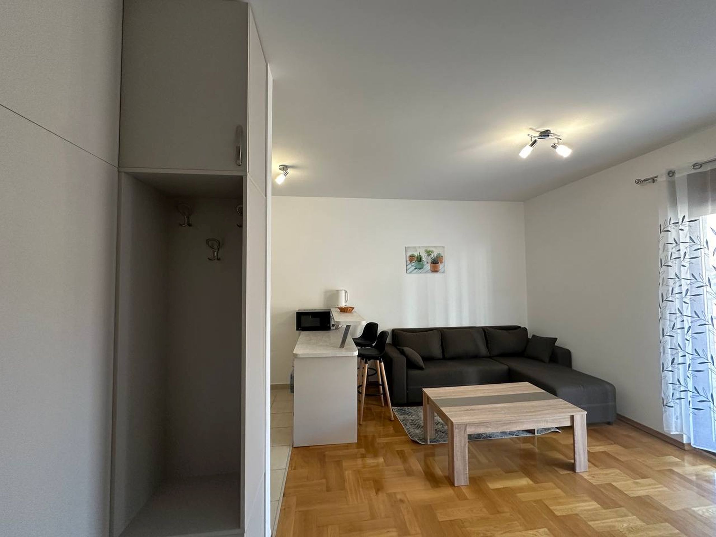 Living room with kitchen in an apartment in Bečići, Montenegro: gray sofa, breakfast bar, and parquet flooring.