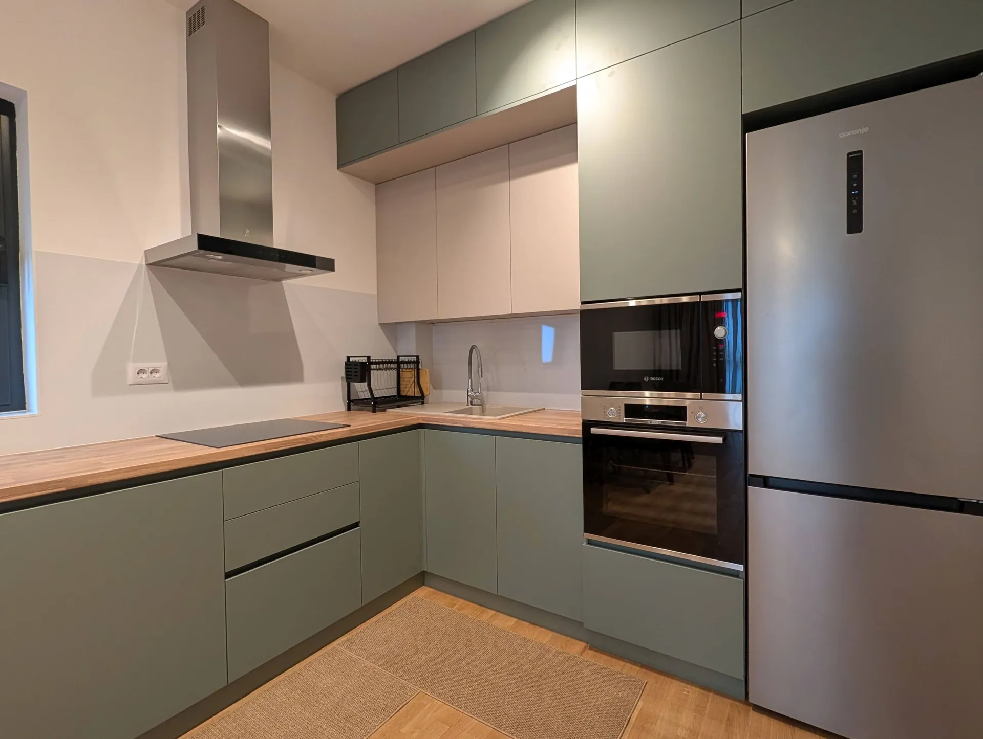 Modern kitchen with green cabinets, wooden countertop, built-in oven, and stainless steel refrigerator.