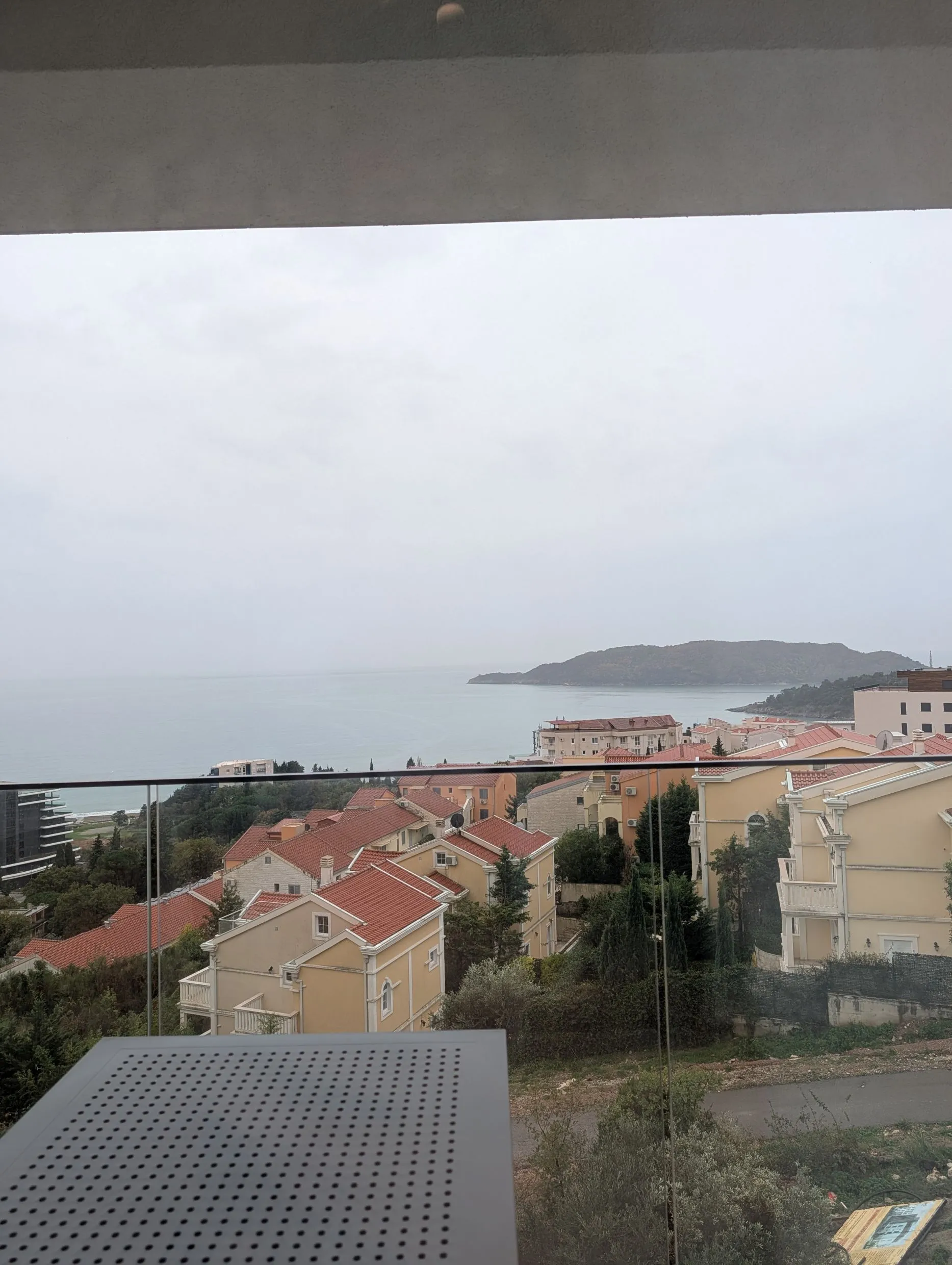 View from a balcony over houses with red roofs and the sea on a cloudy day.