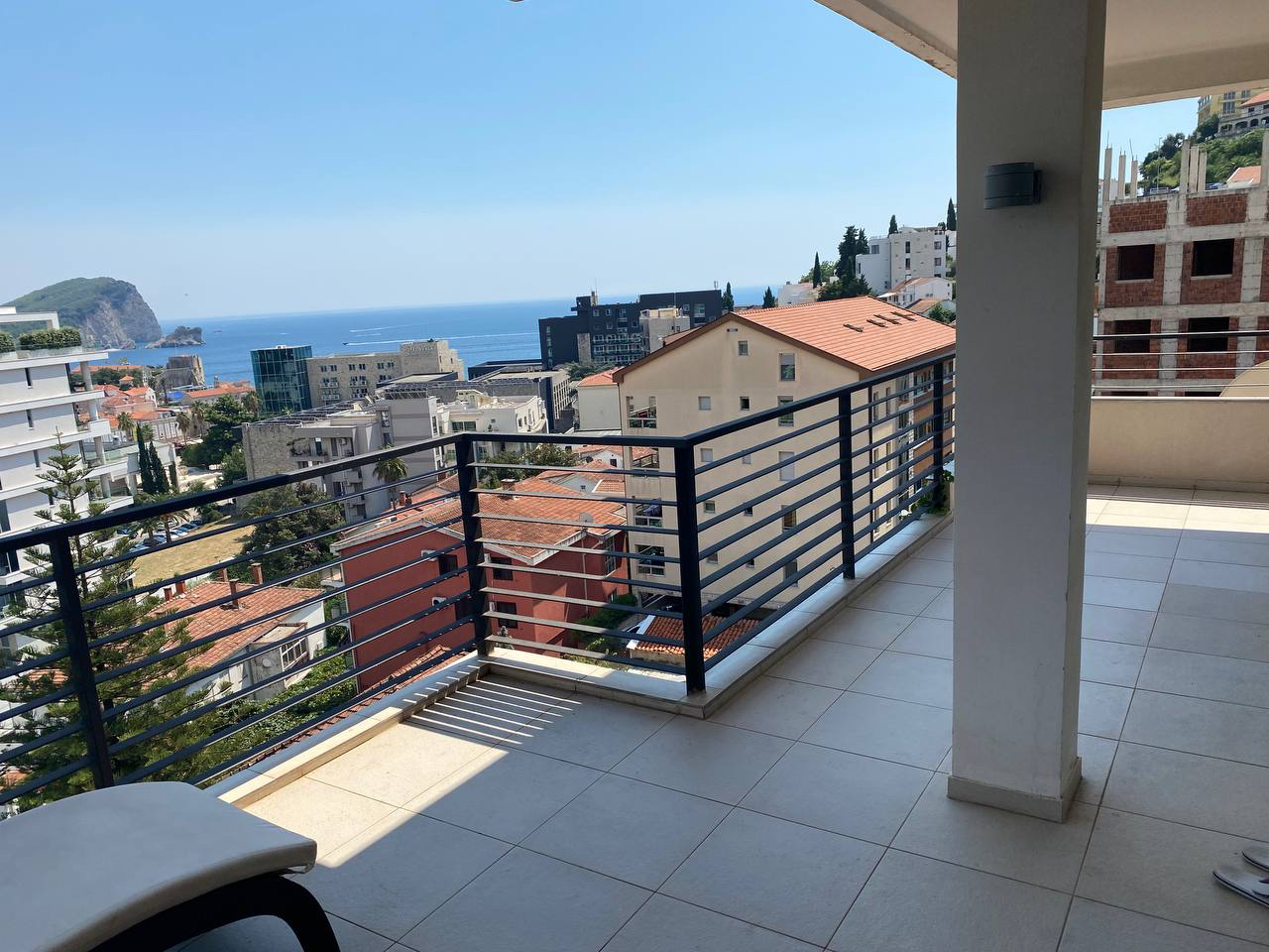 Spacious balcony with panoramic views of the sea and the city of Budva, Montenegro, light tile, and modern railing.