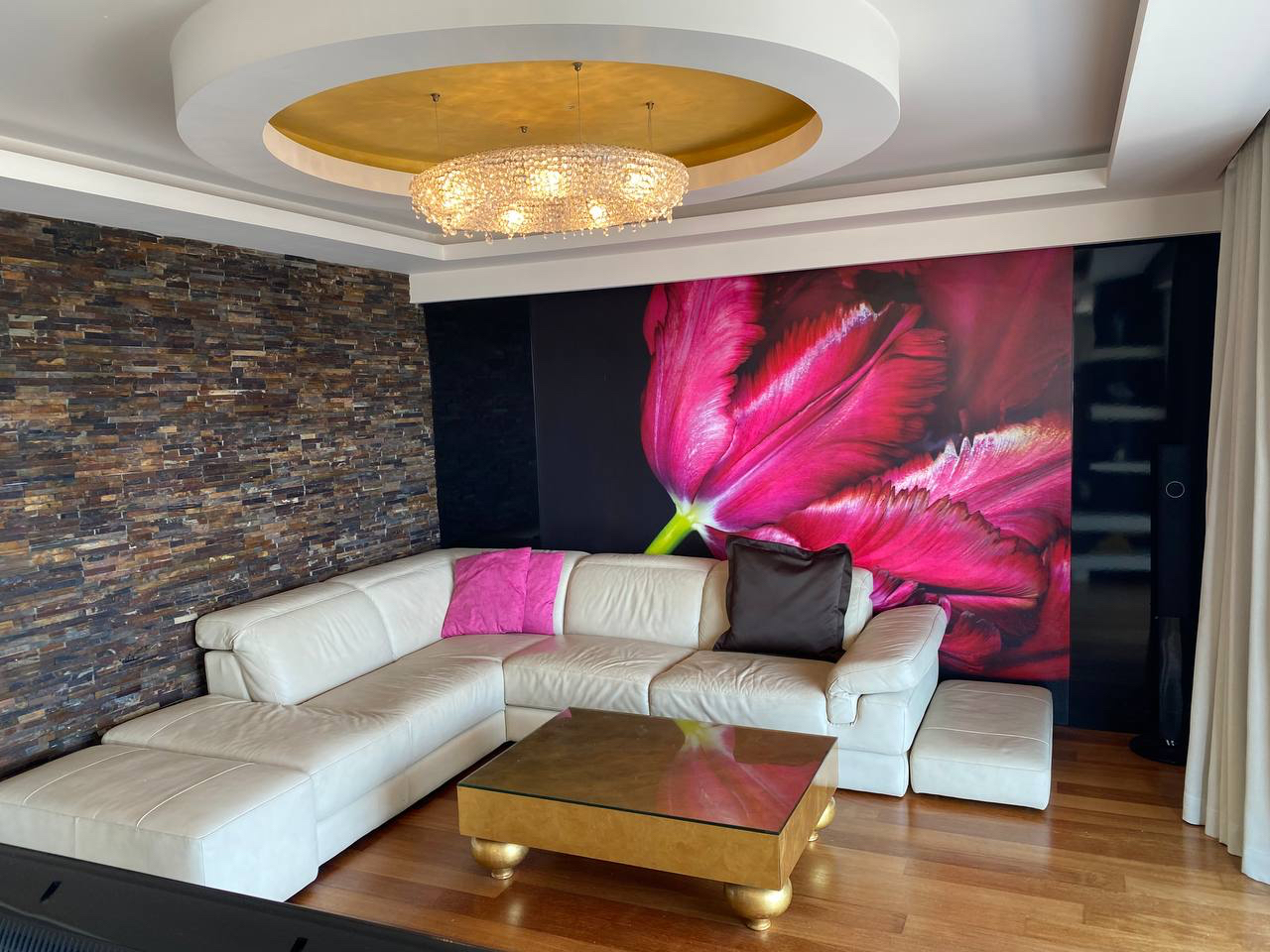 Living room in an apartment in Budva, Montenegro: white leather sofa, stone wall, tulip decor, and a gold ceiling.