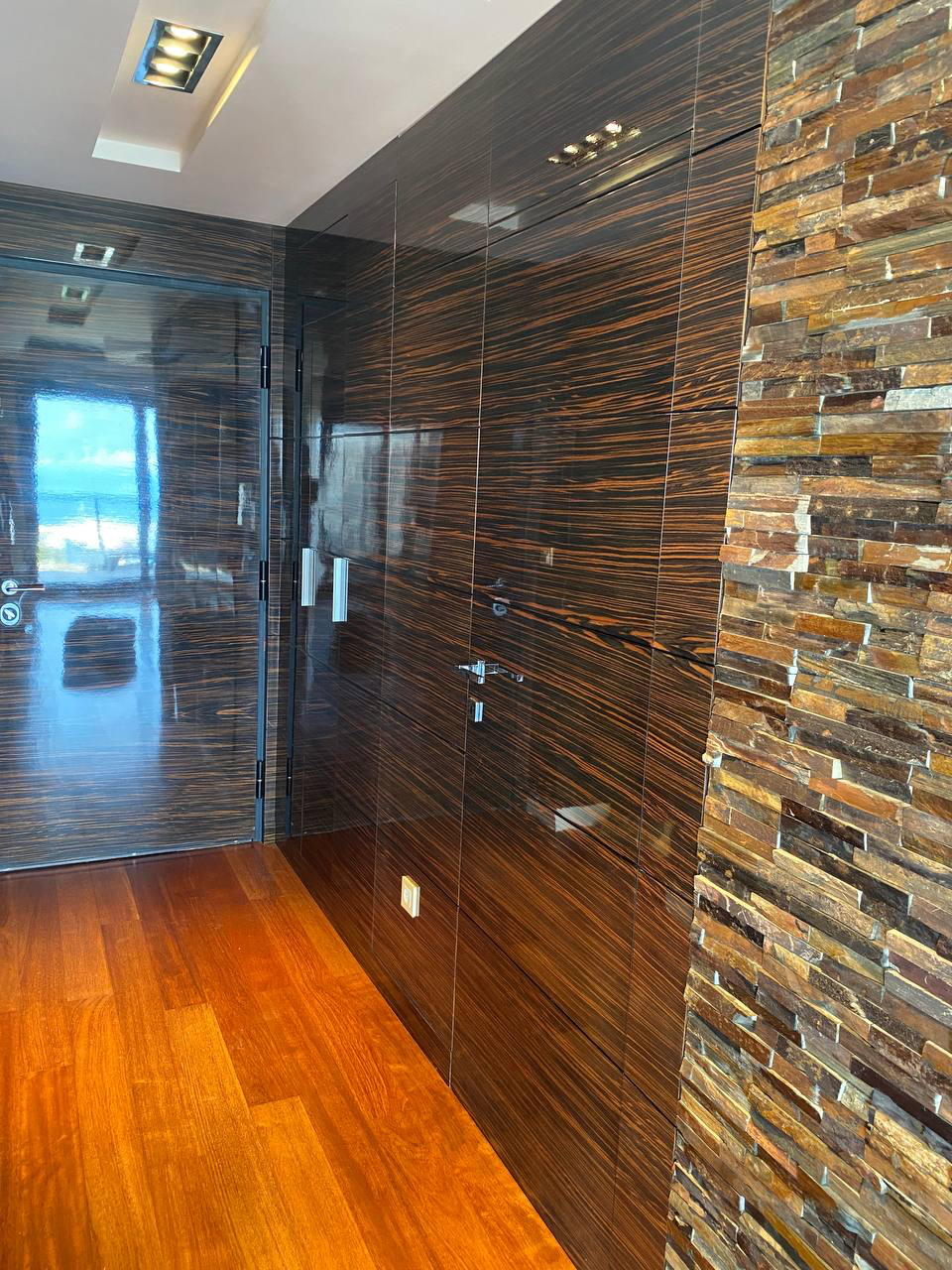 Apartment interior in Budva, Montenegro: glossy wood-look panels, natural stone finishes, and sea view.