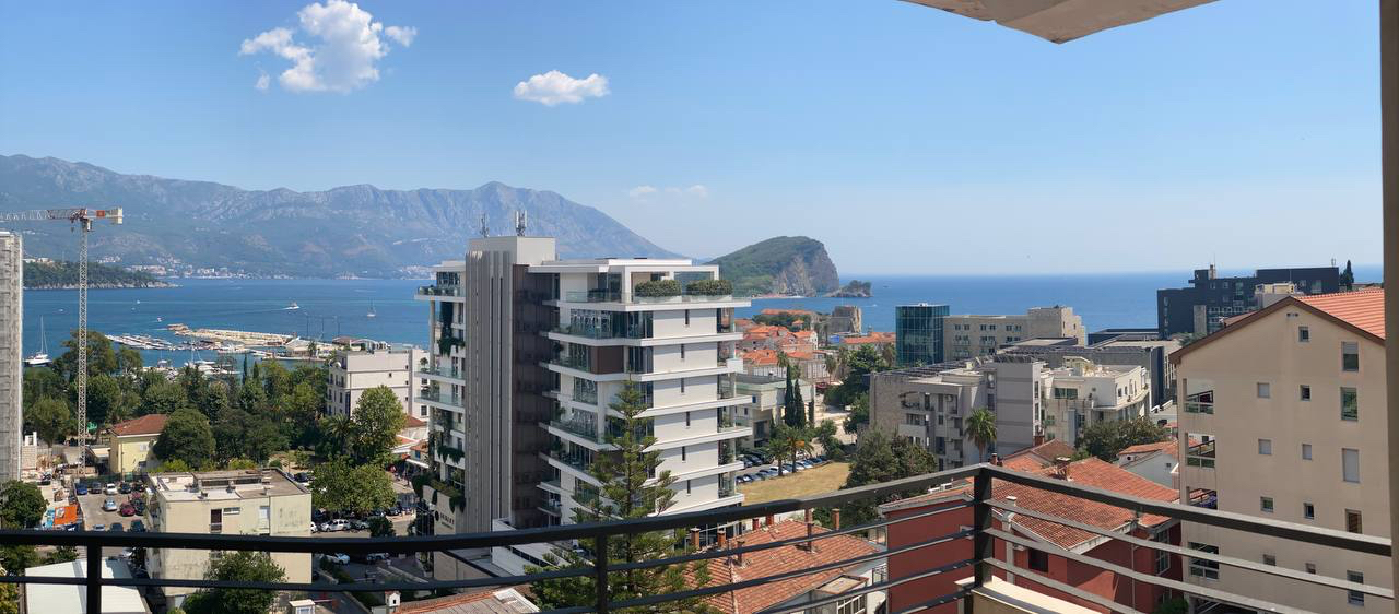 Panoramic view from the apartment balcony in Budva, Montenegro: the sea, St. Nicholas Island, and city buildings.