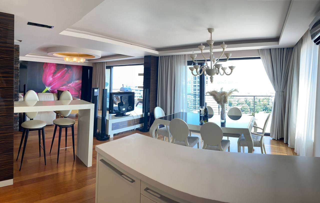 Modern living room with dining area in an apartment in Budva, Montenegro: stylish furniture, panoramic windows, and sea view.