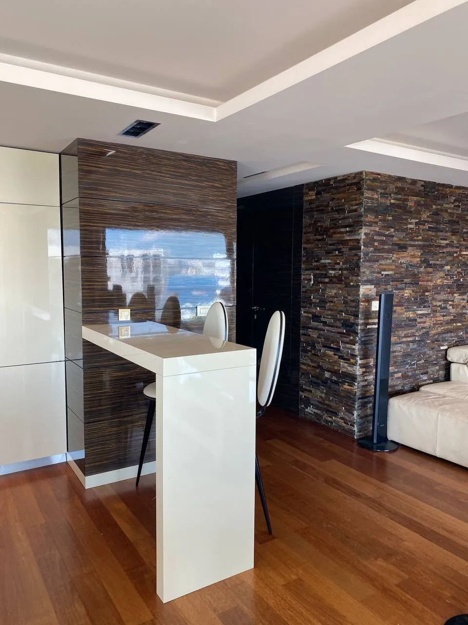 Modern living room with a white bar counter, wooden floor, and decorative stacked stone wall.
