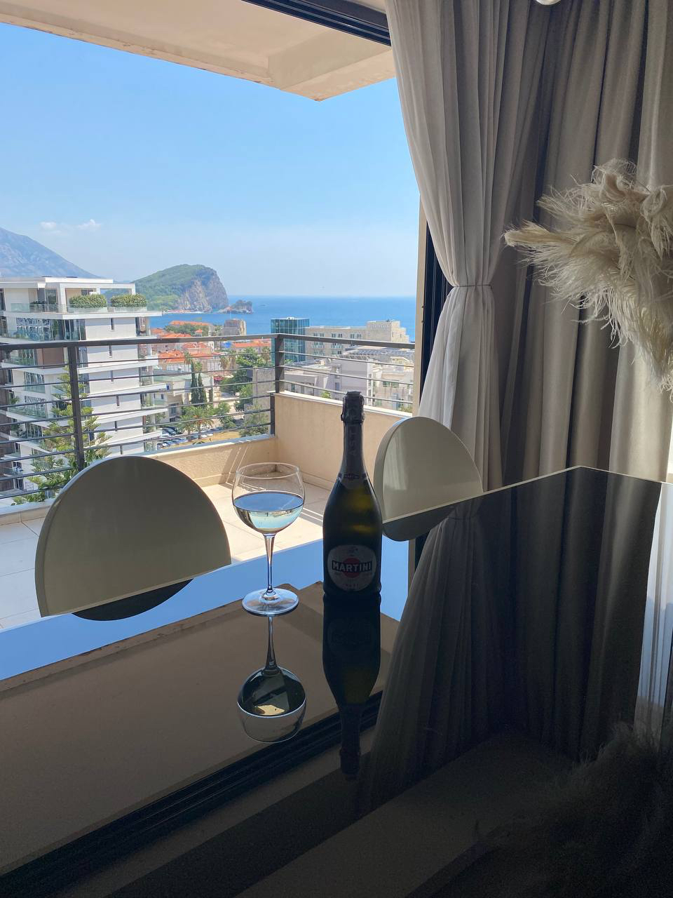 Sea and mountain view from the living room of a modern apartment in Budva, Montenegro: dining table with a bottle of champagne and a terrace.