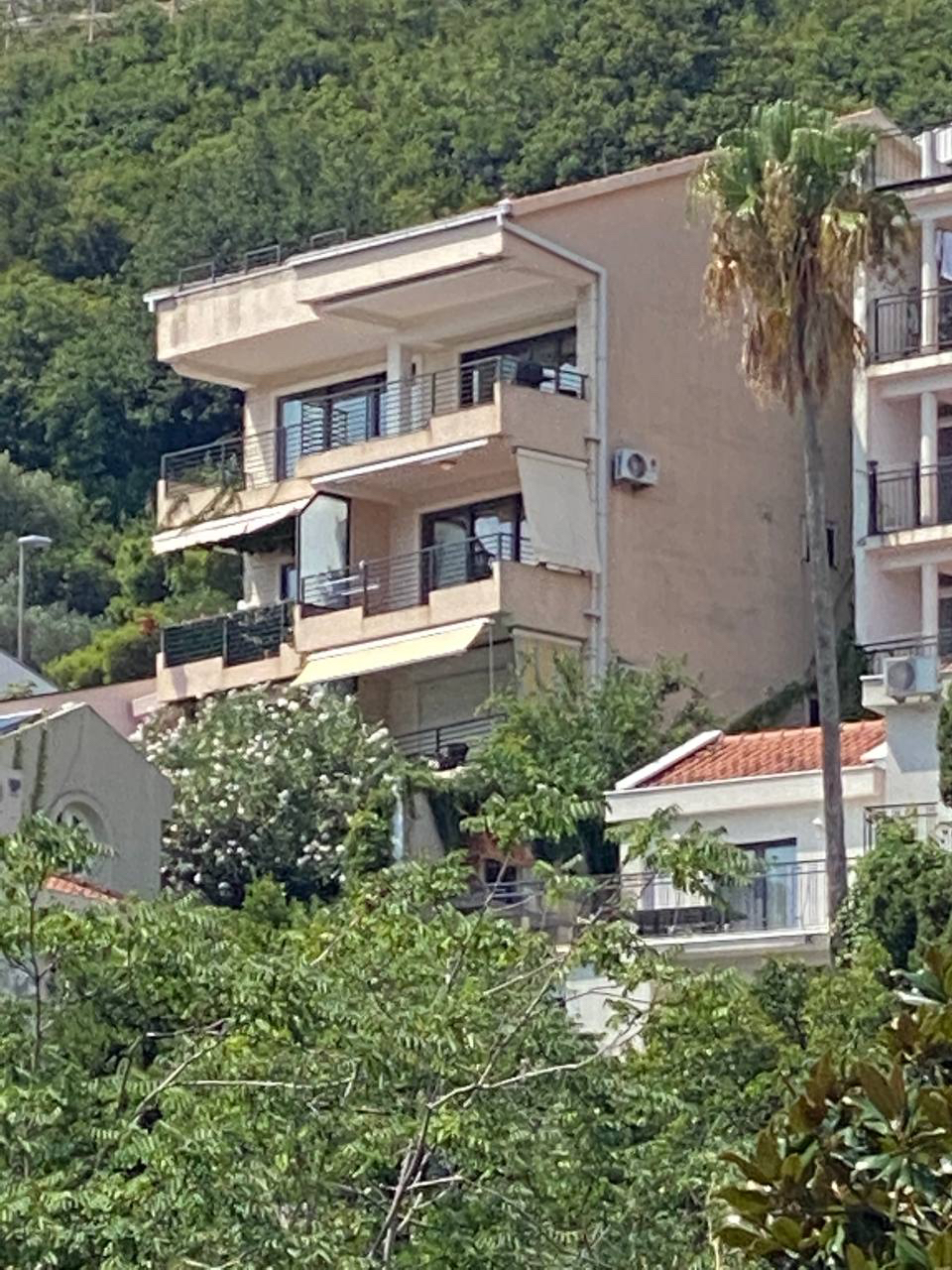 Facade of an apartment building with balconies and a palm tree in Budva, Montenegro: view of a residential complex surrounded by greenery.
