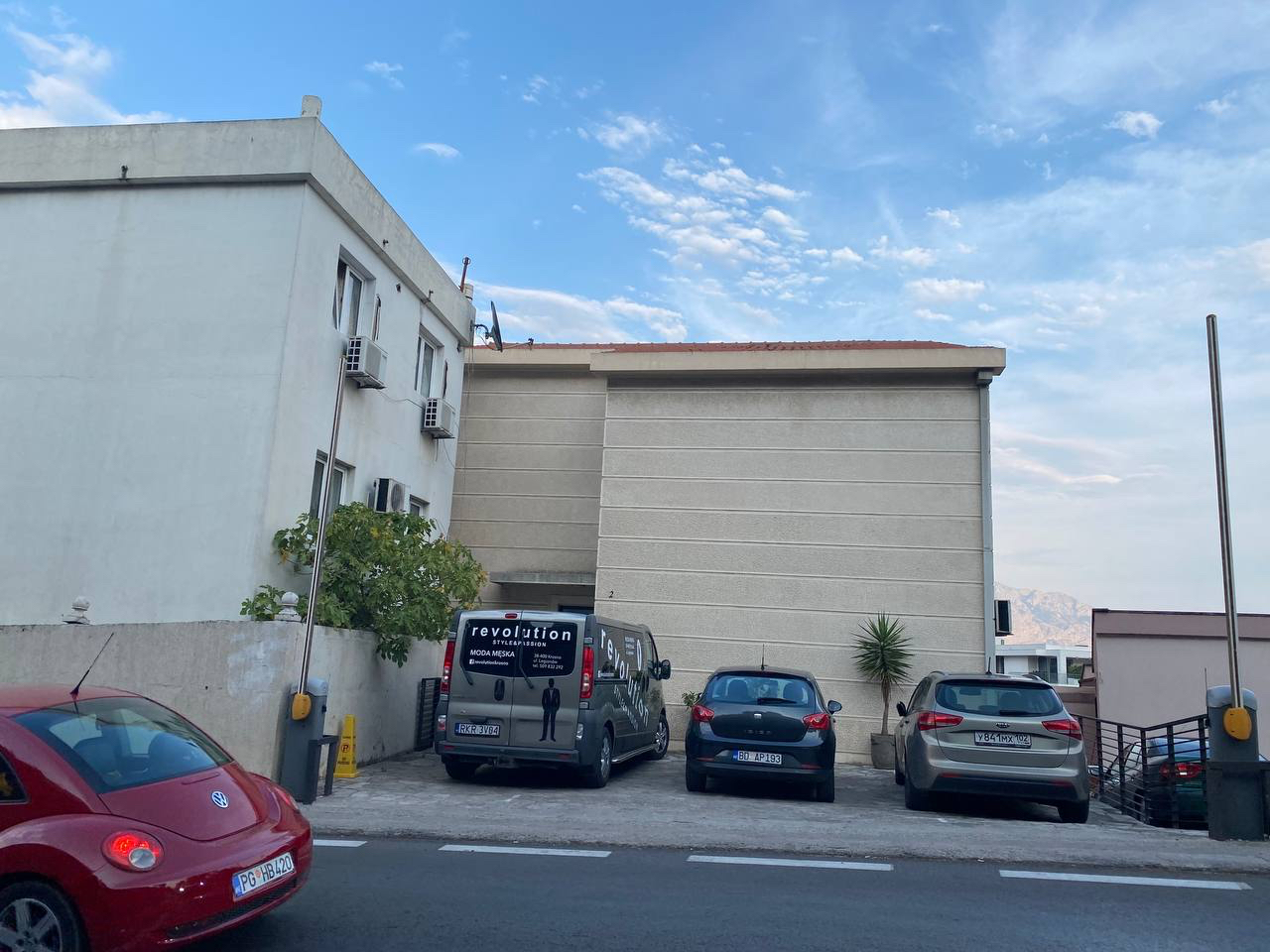 Facade of a residential building in Budva, Montenegro, with parking for cars at the entrance and mountain views.