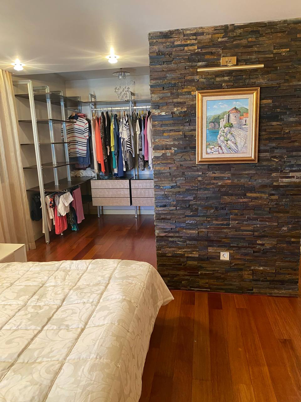 Bedroom in an apartment in Budva, Montenegro: open wardrobe, decorative stone wall finish, and parquet flooring.