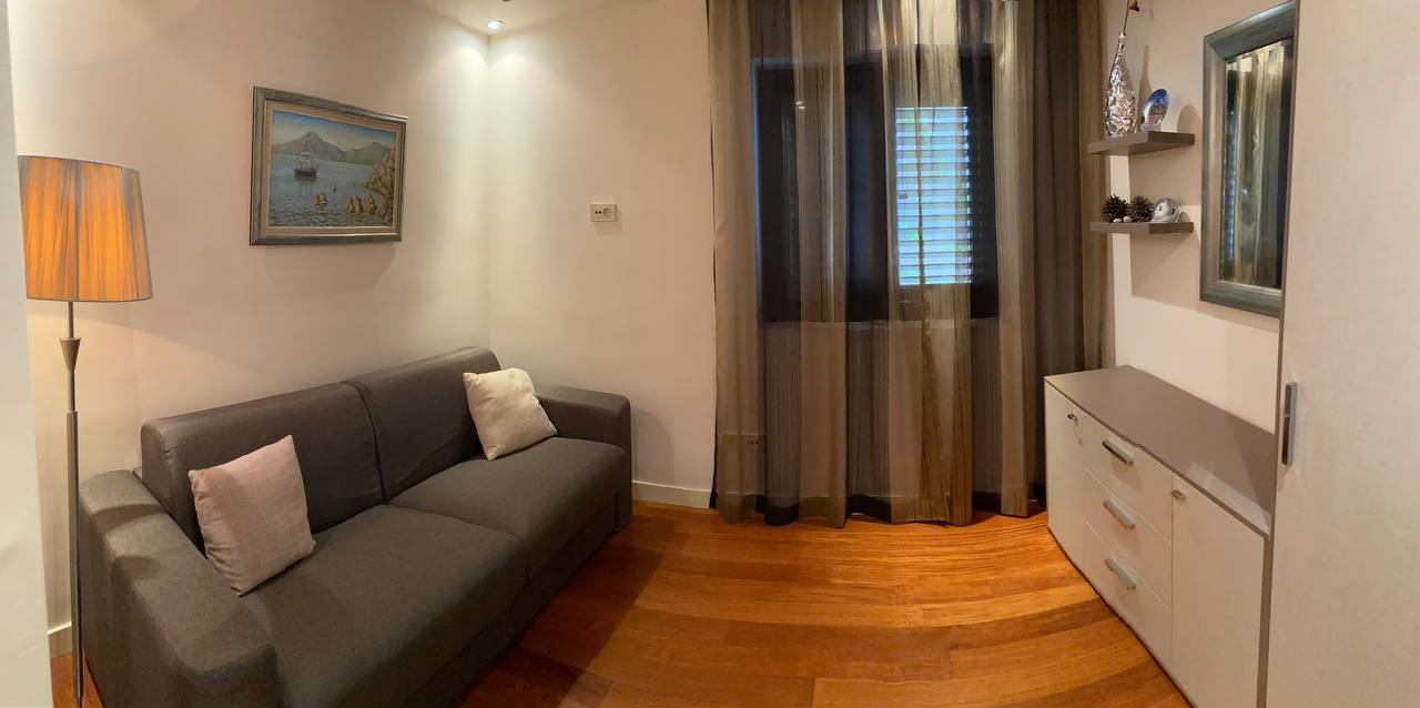 Cozy living room with a gray sofa and parquet flooring in an apartment for sale in Budva, Montenegro. Modern interior.