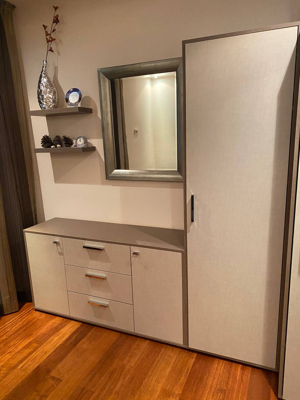 Modern furniture in the bedroom of an apartment in Budva, Montenegro: a light-colored wardrobe, dresser, mirror, and shelves with decor.