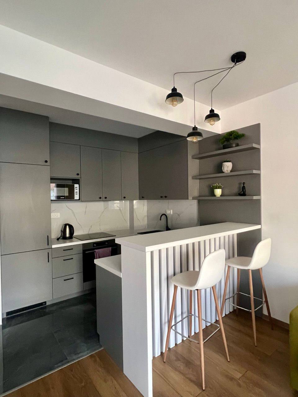 Modern kitchen in an apartment in Budva, Montenegro: gray cabinetry, a bar counter with stools, and stylish lighting.