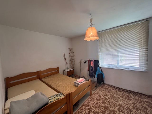 Bedroom in a house in Dobra Voda, Montenegro: two wooden beds, a patterned rug, a window with blinds, and a vintage chandelier.