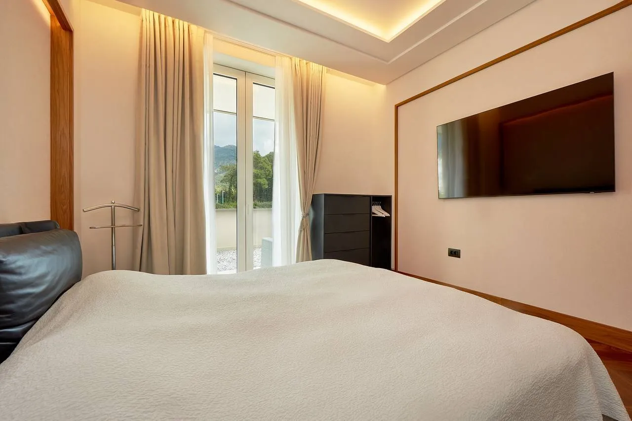 Modern bedroom featuring a large bed, wall-mounted TV, and balcony with a scenic mountain view.