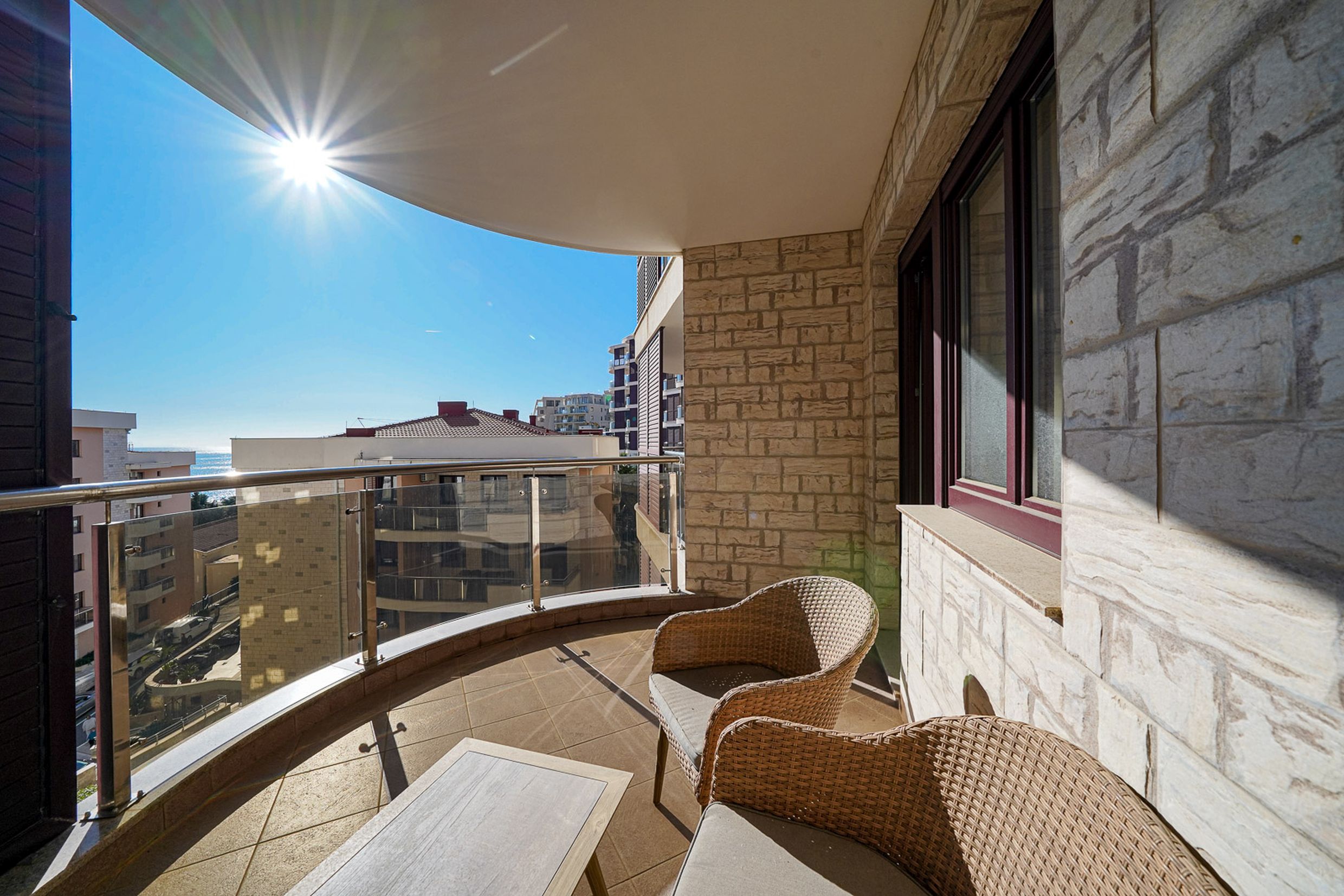 Cozy balcony with wicker furniture and a sea view in an apartment in Becici, Montenegro. Natural stone finish.