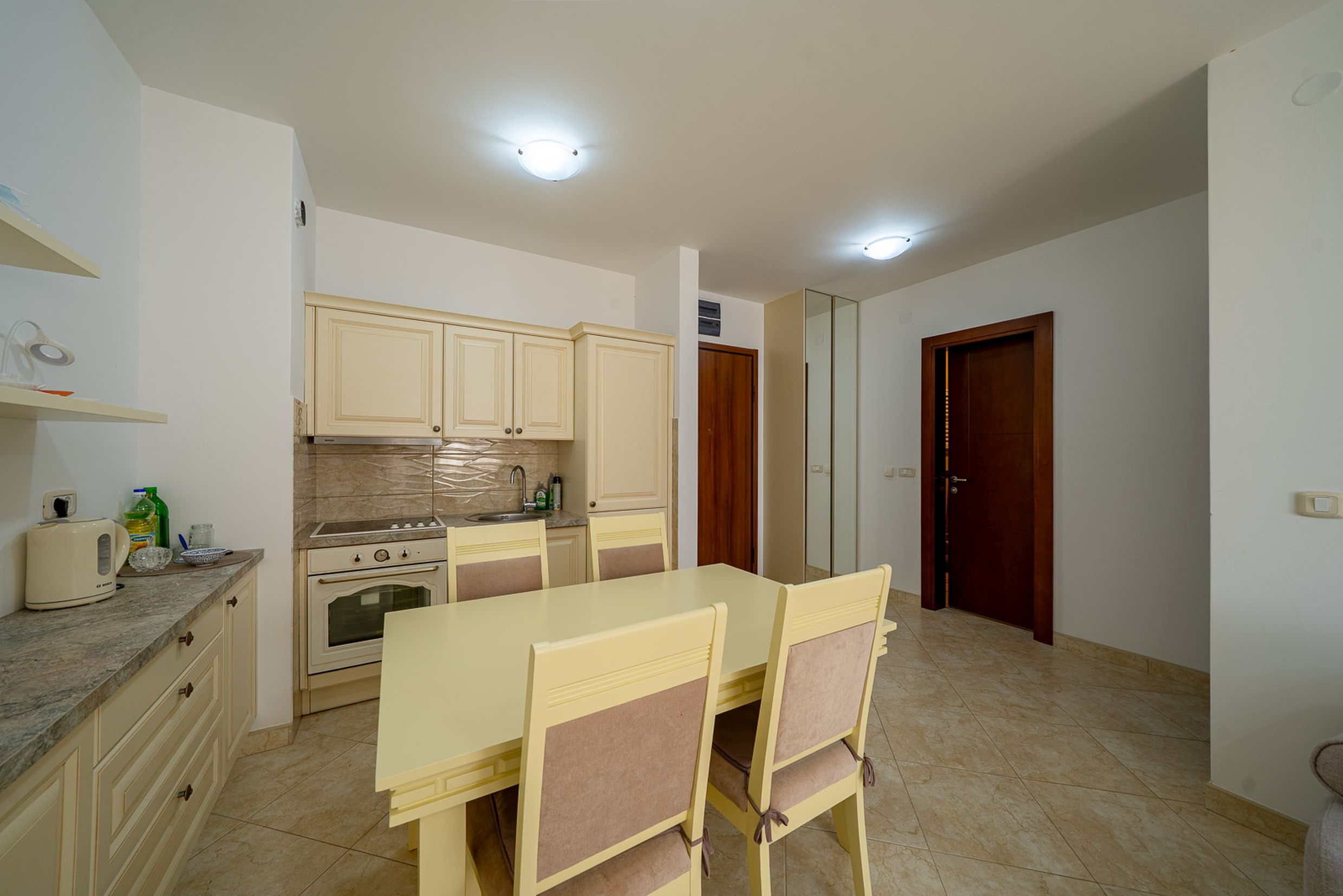 Kitchen-dining room with light-colored cabinetry in an apartment in Bečići, Montenegro. Dining area with classic-style furniture.