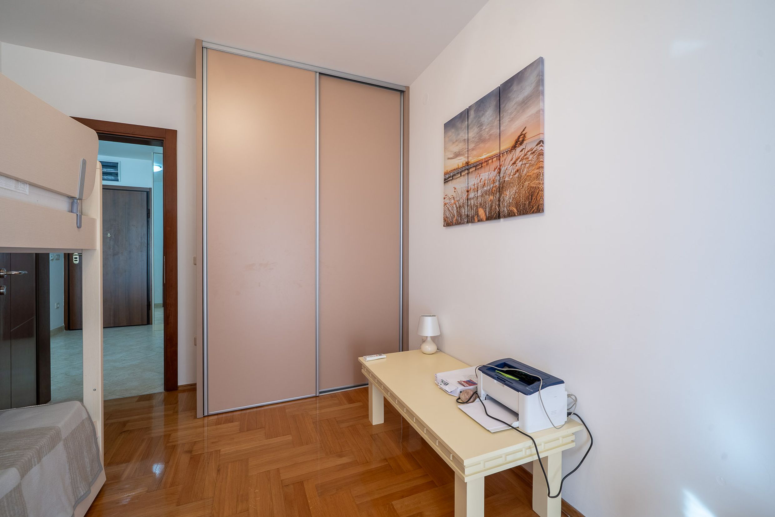 Bedroom in an apartment in Bečići, Montenegro: built-in sliding-door wardrobe, parquet flooring, desk with a printer, and decor.