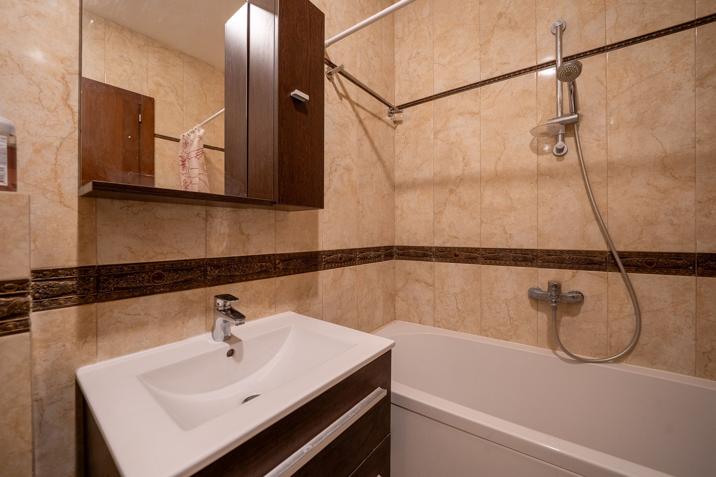Bathroom in an apartment in Bečići, Montenegro: white sanitary ware, vanity unit with a sink, and beige decorative tiles.
