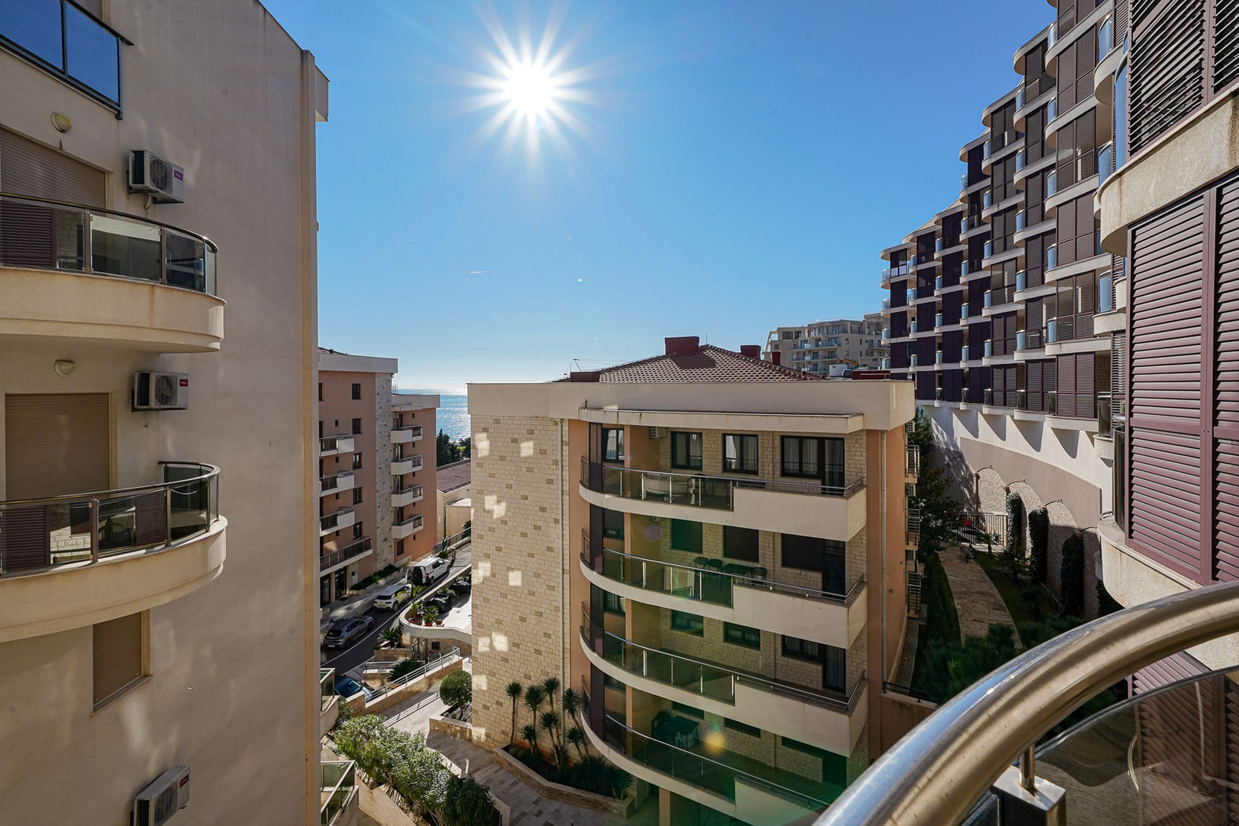 View from the balcony of an apartment in Bečići, Montenegro: modern residential buildings, sunny weather, and a partial sea view.
