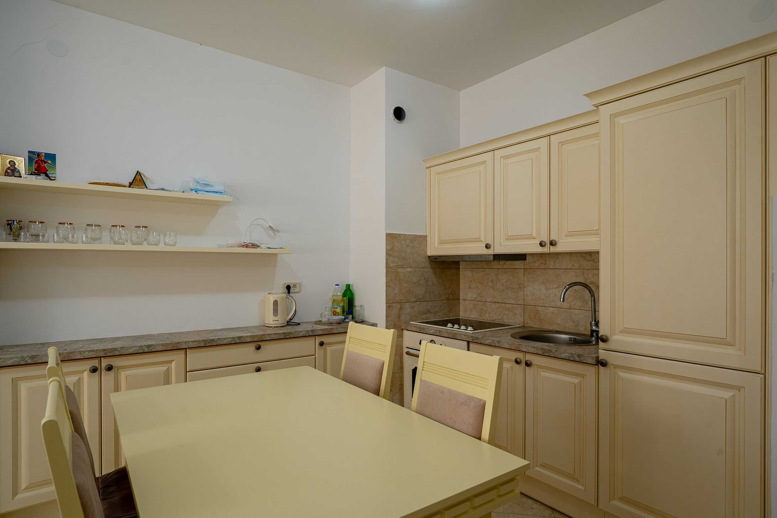 Bright kitchen with a dining area in an apartment, Becici, Montenegro: beige cabinetry, built-in appliances, and a dining table.