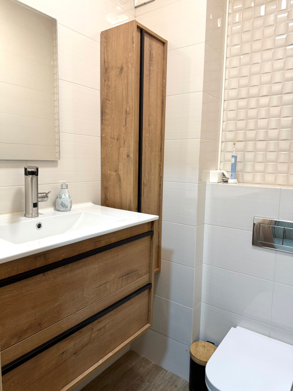Modern bathroom in an apartment, Podgorica, Montenegro: light tiles, wood-look furniture, wall-hung fixtures.