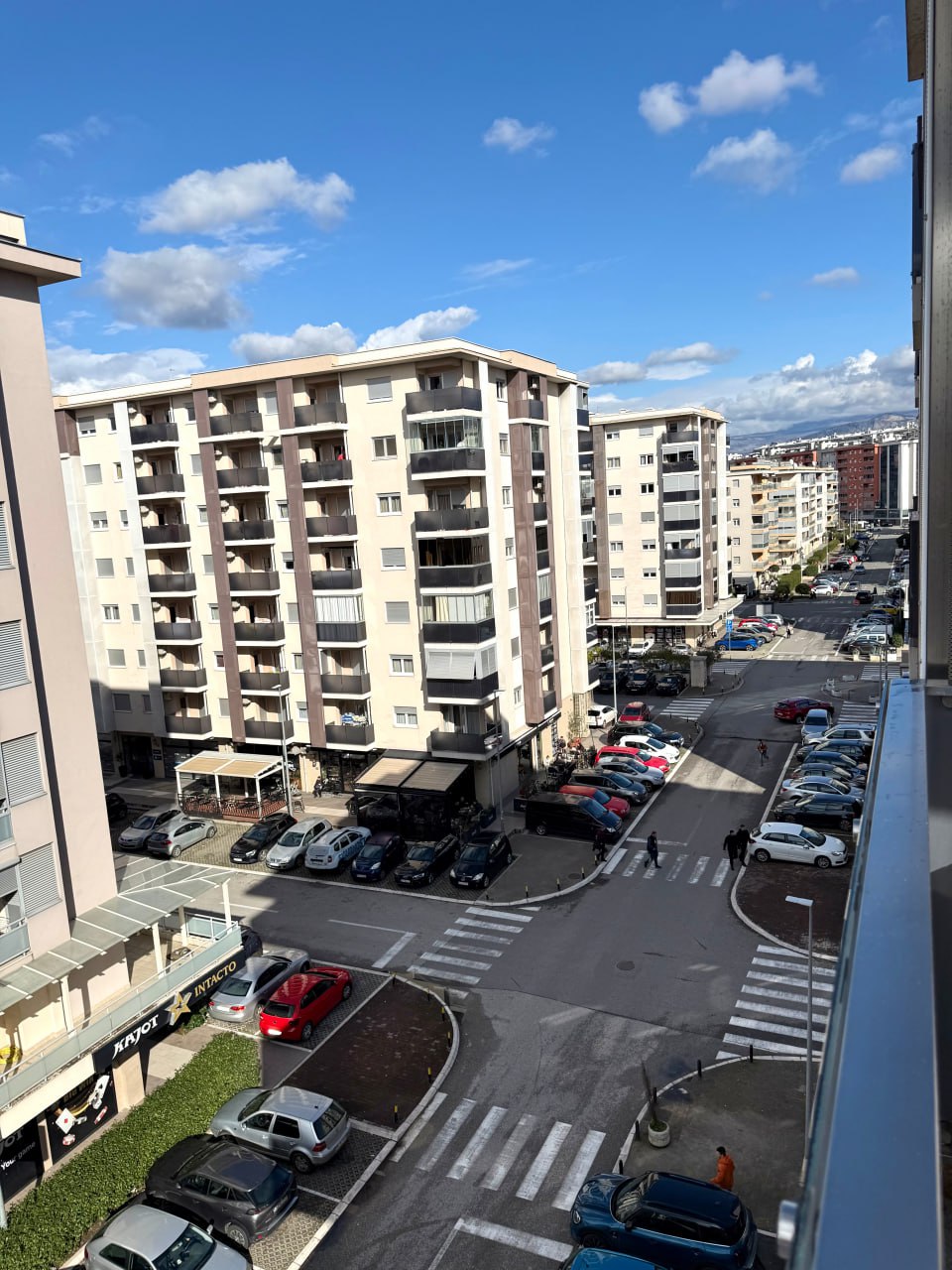 View from the apartment window in Podgorica, Montenegro: urban development, a residential block, and a parking lot near the house on a sunny day.