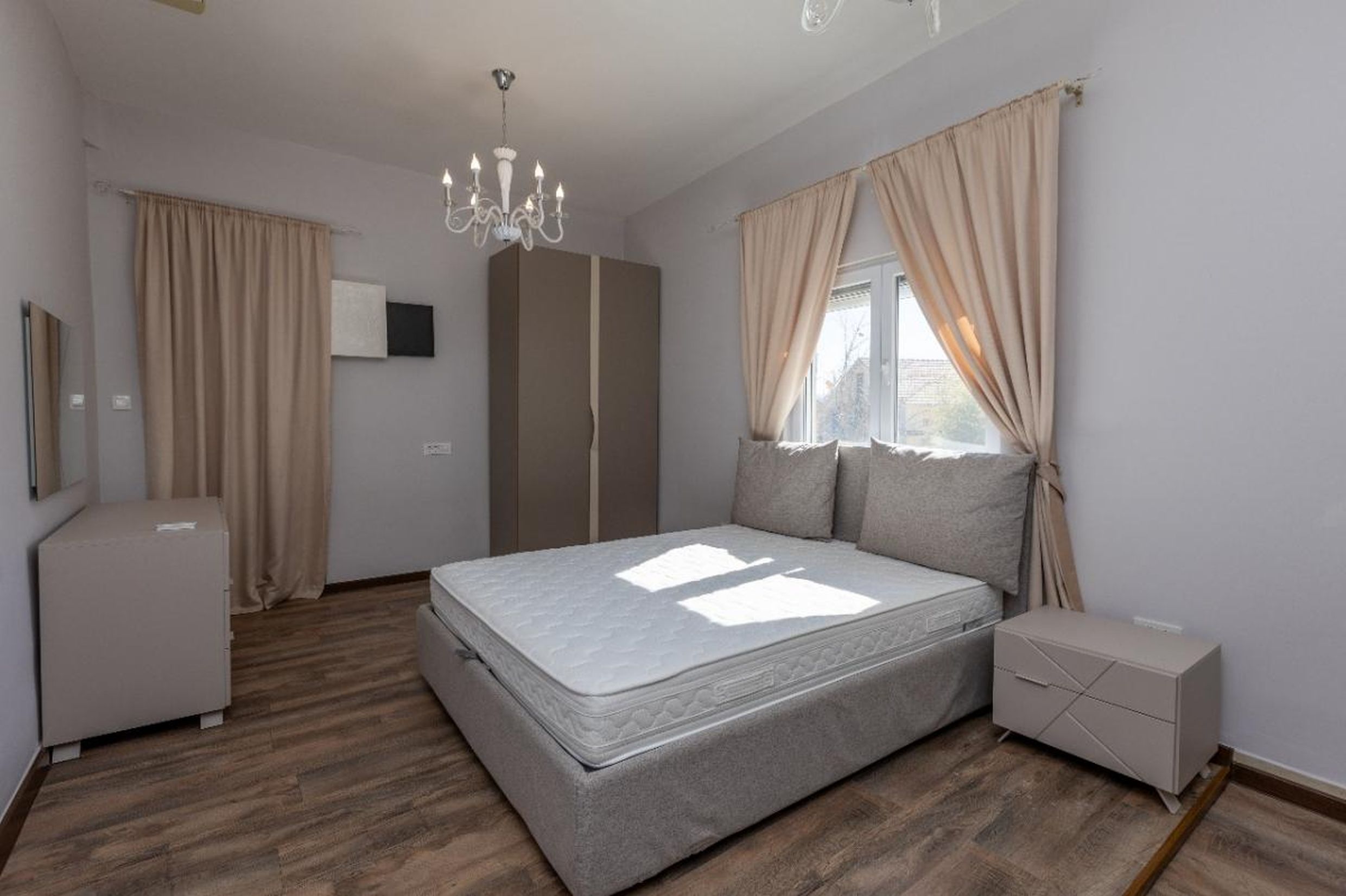 Bright bedroom in a house in Tivat, Montenegro: double bed, wardrobe, dresser, laminate flooring, and a classic chandelier.