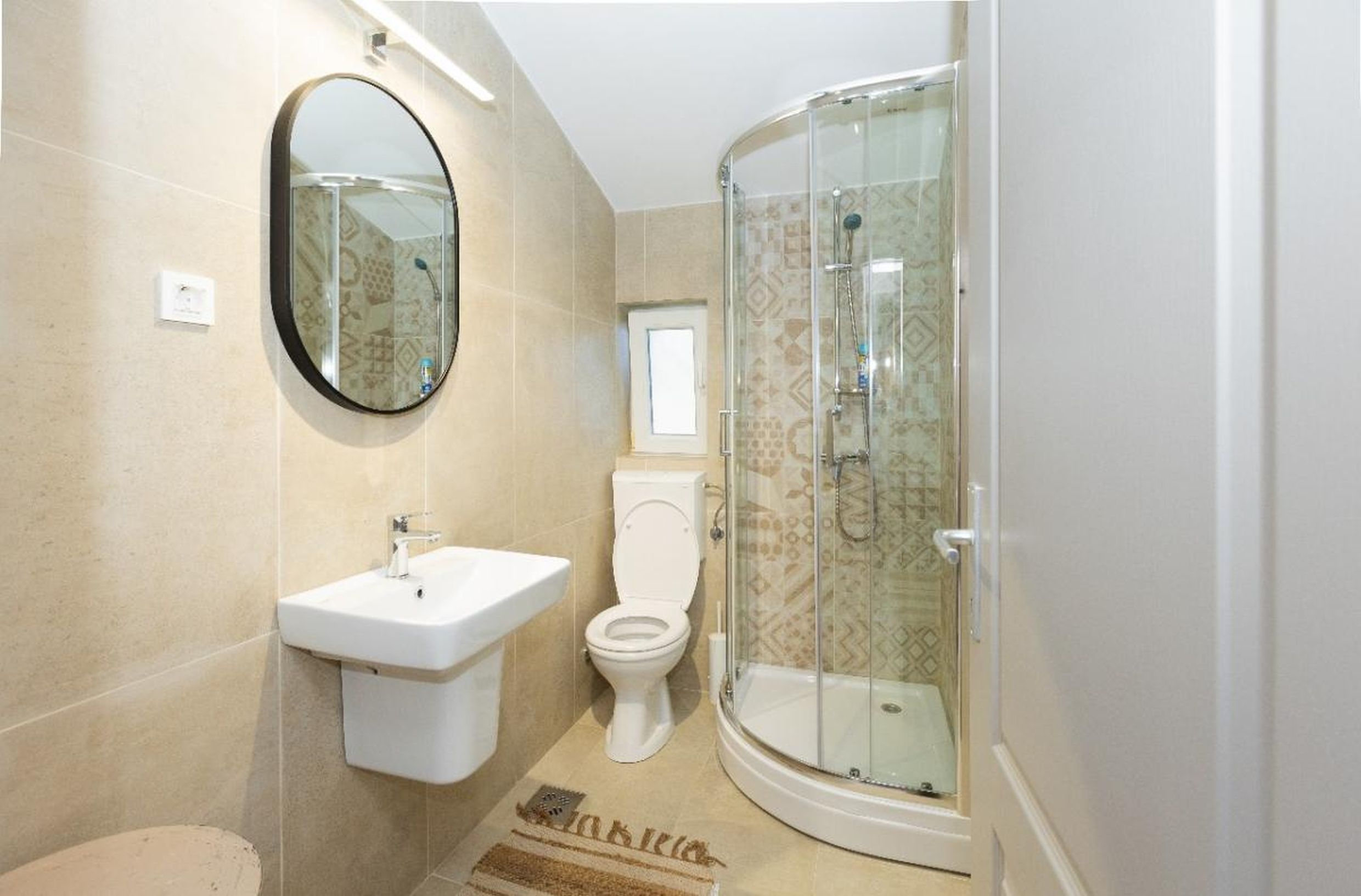 Modern bathroom with a shower cabin in a house, Tivat, Montenegro: beige tiles and a round mirror.