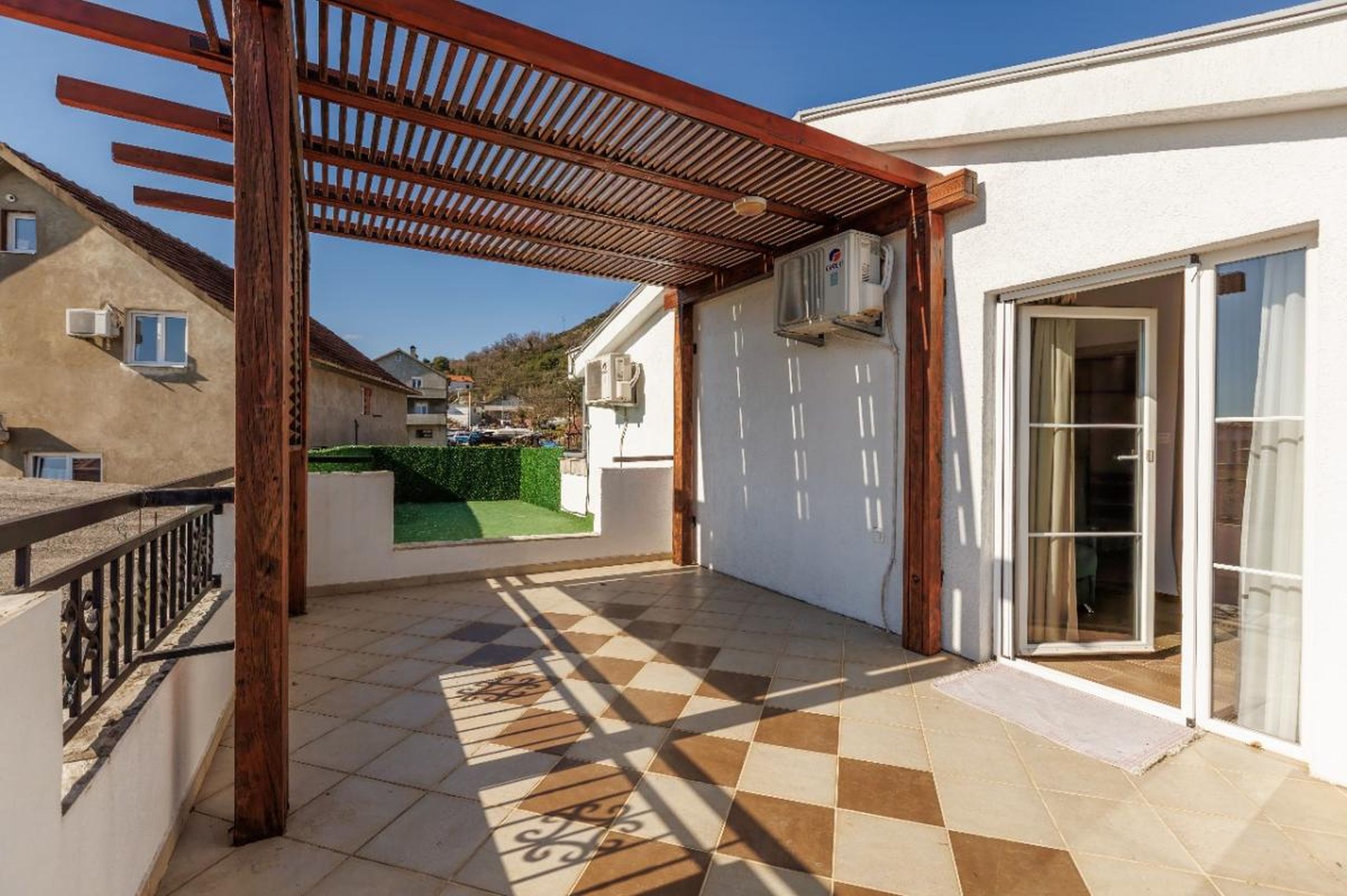 Spacious terrace with a wooden canopy and tiled floor in a house, Tivat, Montenegro. View of the mountains and residential area.