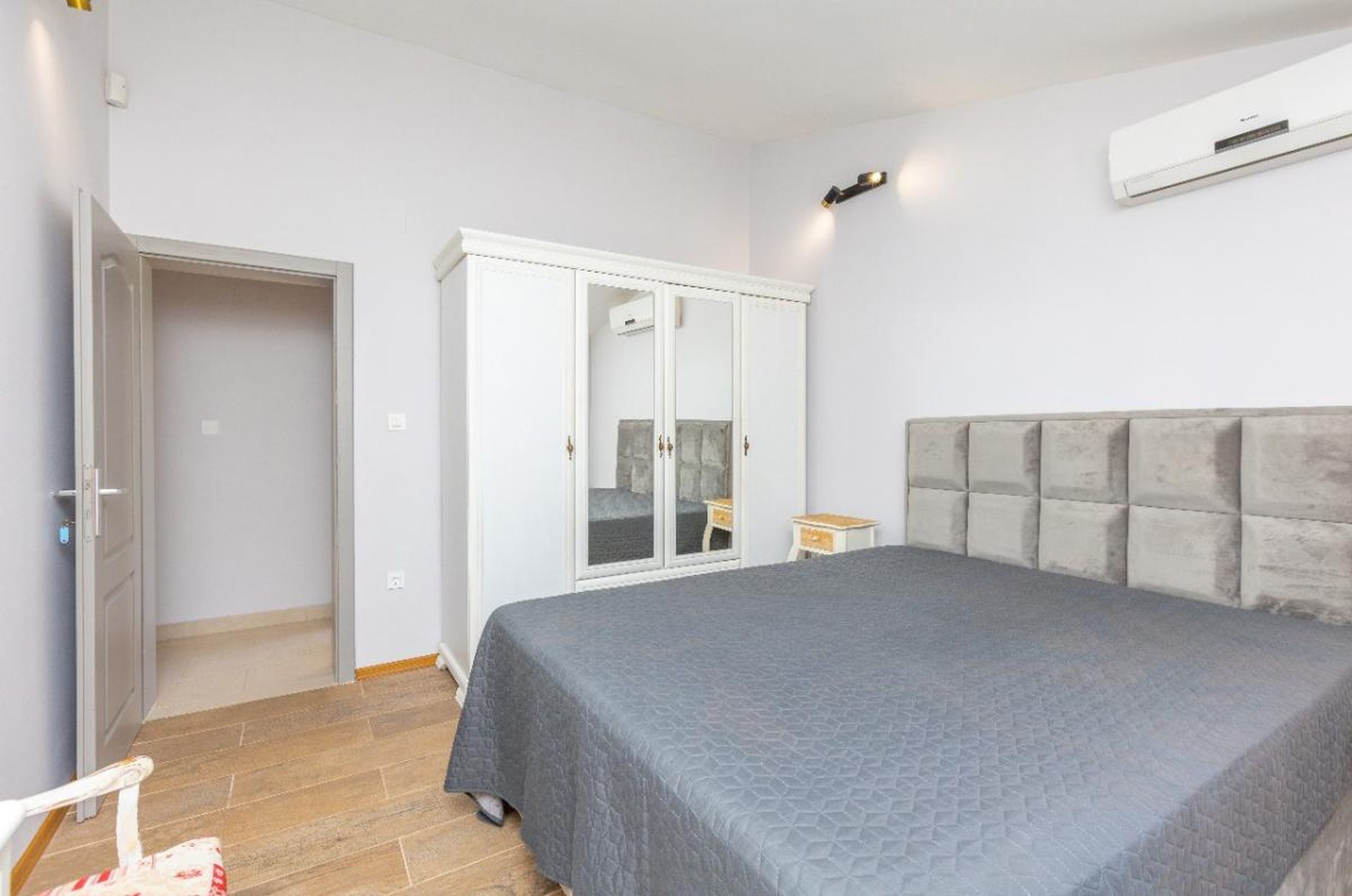 Bright bedroom in a house in Tivat, Montenegro: a double bed with a padded headboard, a white wardrobe, and air conditioning.