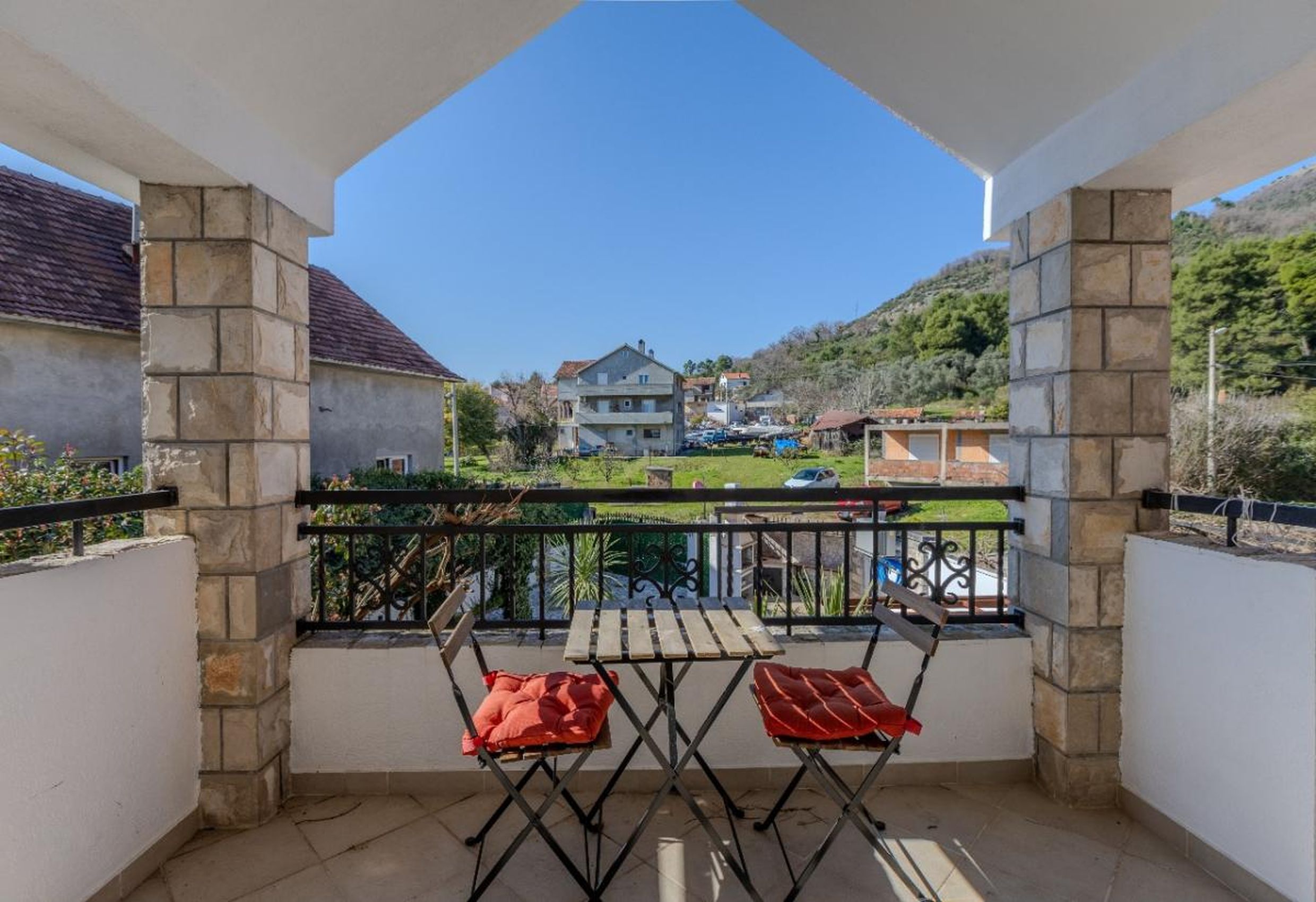 Balcony with stone columns and mountain views in a house in Tivat, Montenegro, with a table and two chairs.
