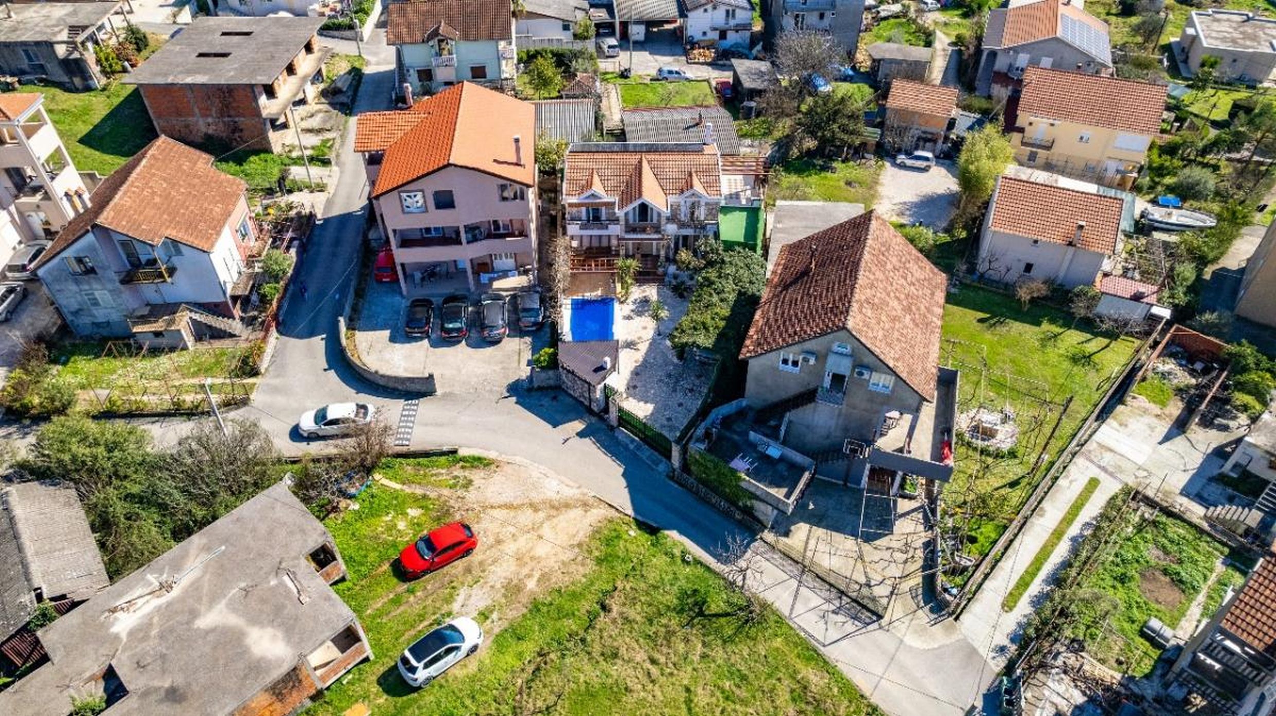 Aerial view of private houses with tiled roofs and a swimming pool in Tivat, Montenegro, with parking area.