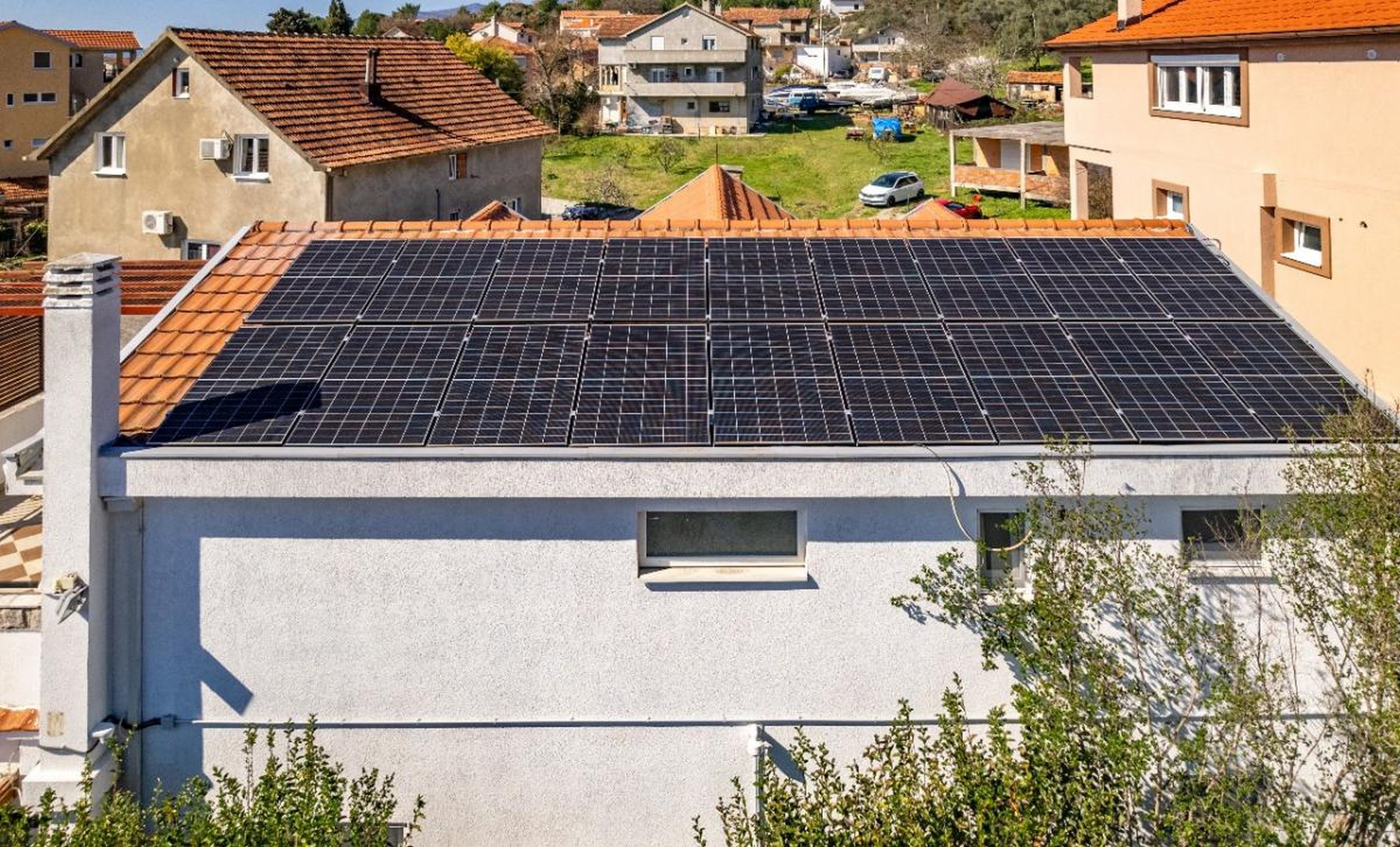 Modern solar panels on the roof of a private house in Tivat, Montenegro, overlooking a residential area with tiled roofs.
