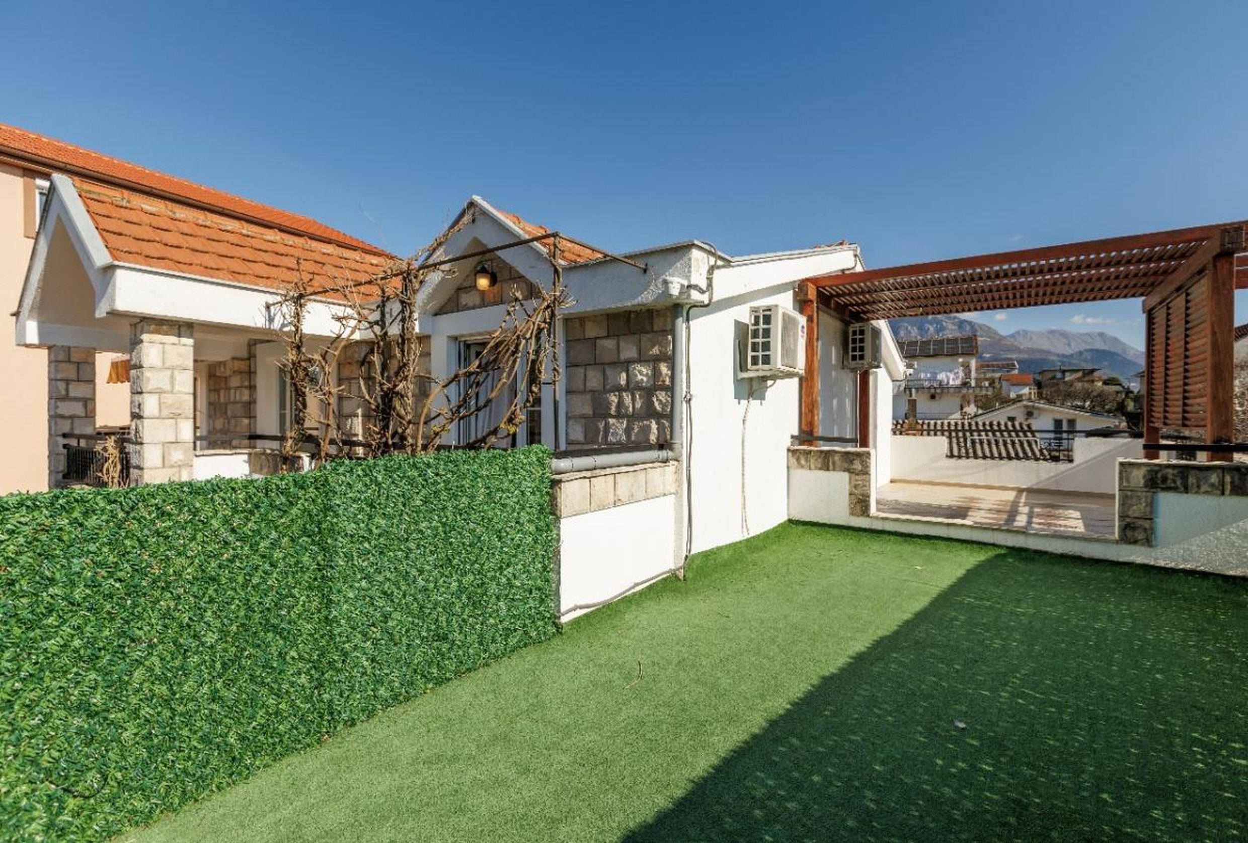 House terrace in Tivat, Montenegro: artificial grass, wooden pergola, stone finishes, and mountain views.