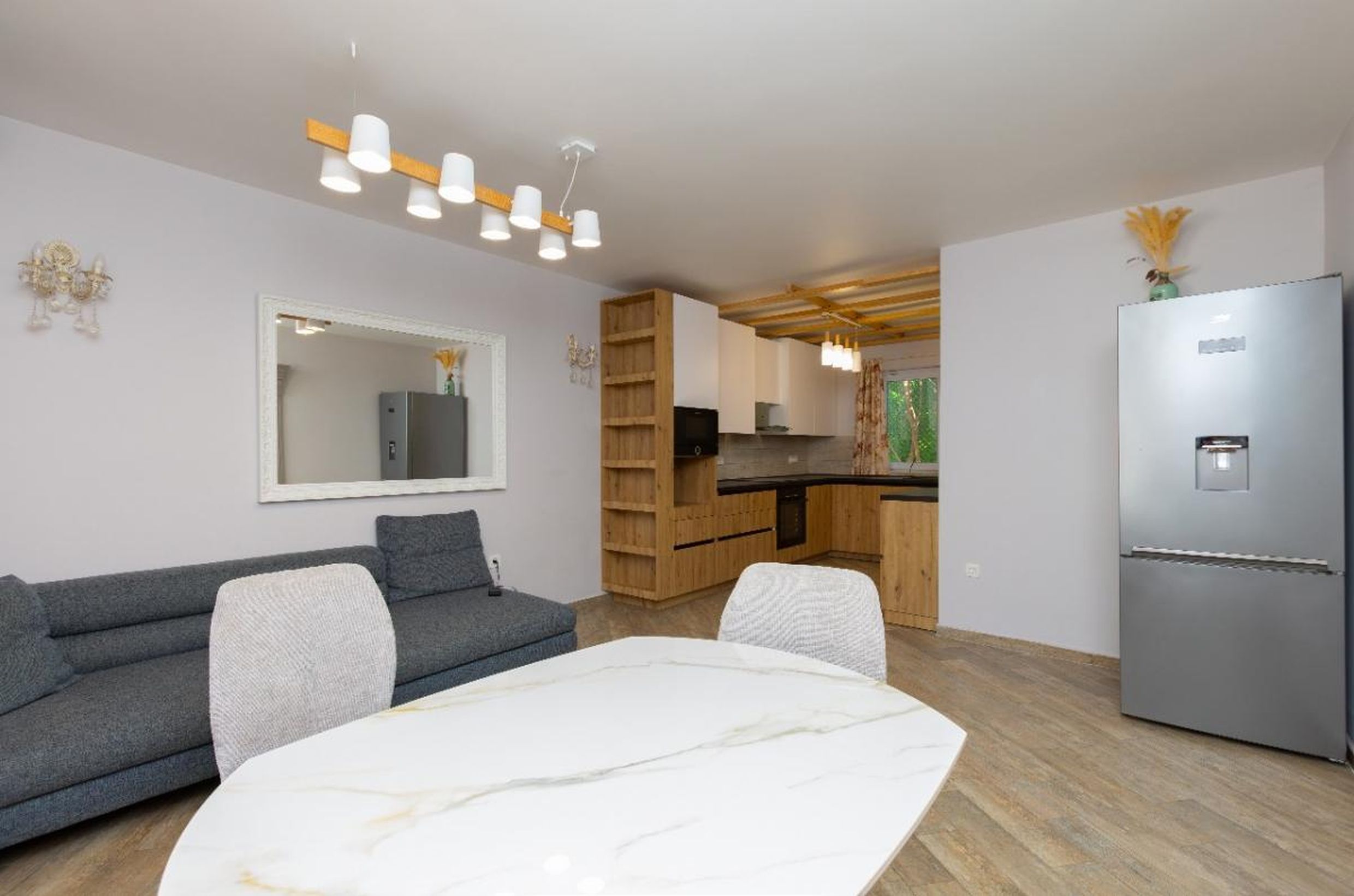 Modern living room with kitchen in a house in Tivat, Montenegro: gray sofa, marble table, and built-in wooden furniture.