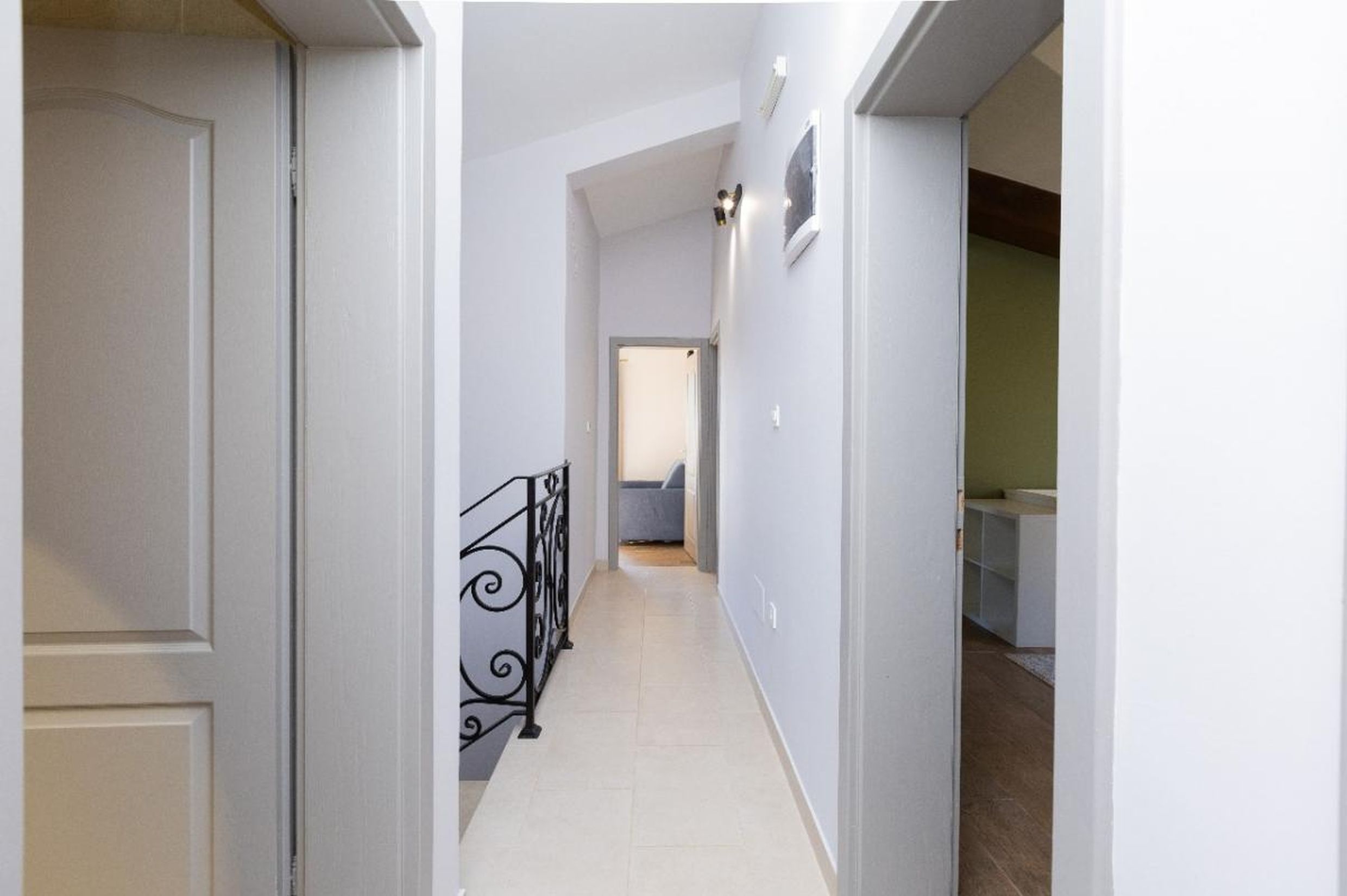Bright hallway in a house in Tivat, Montenegro: wrought-iron staircase railing, tiled floor, and interior doors.