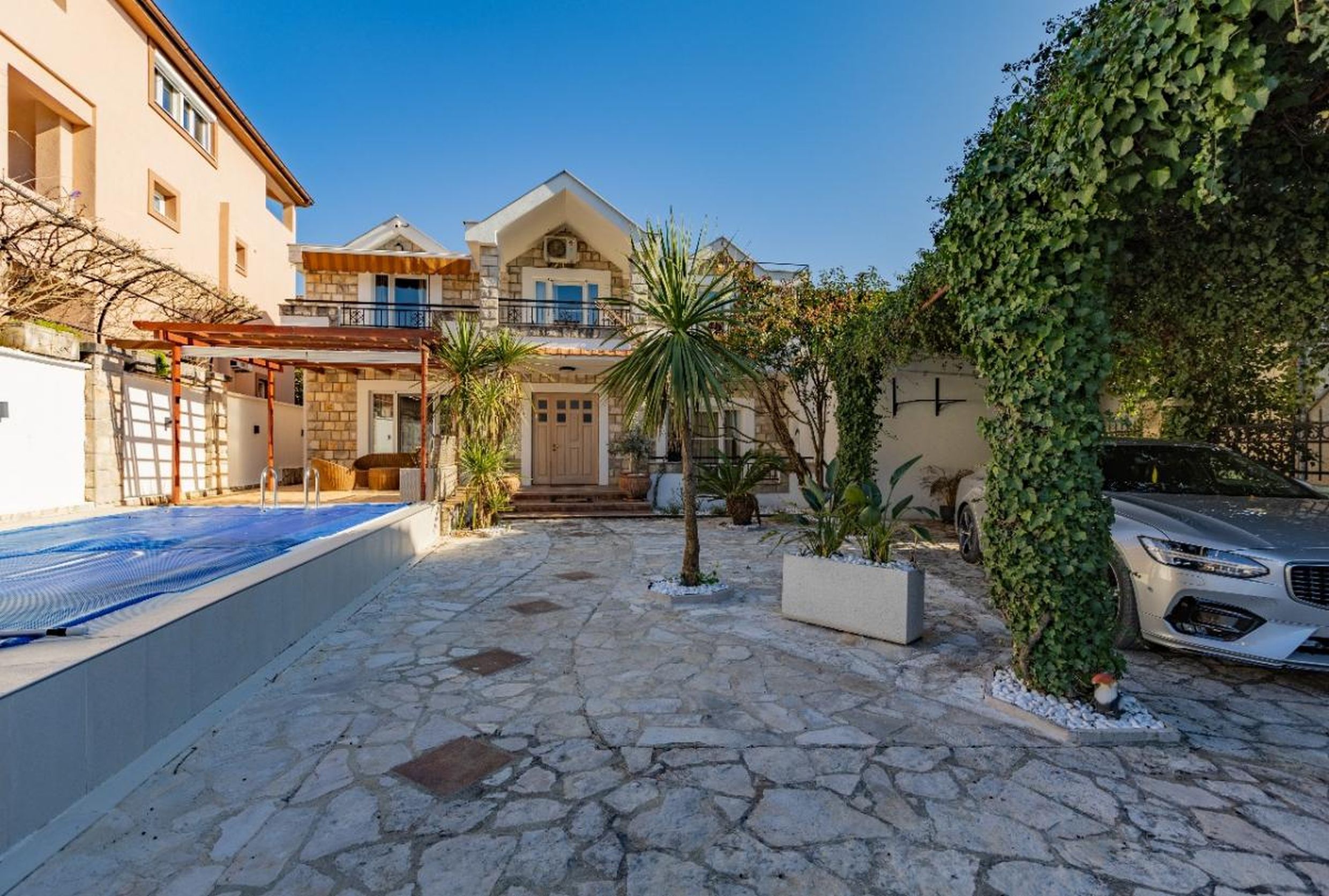 Two-story villa in Tivat, Montenegro: stone facade, private pool, terrace, and courtyard parking.