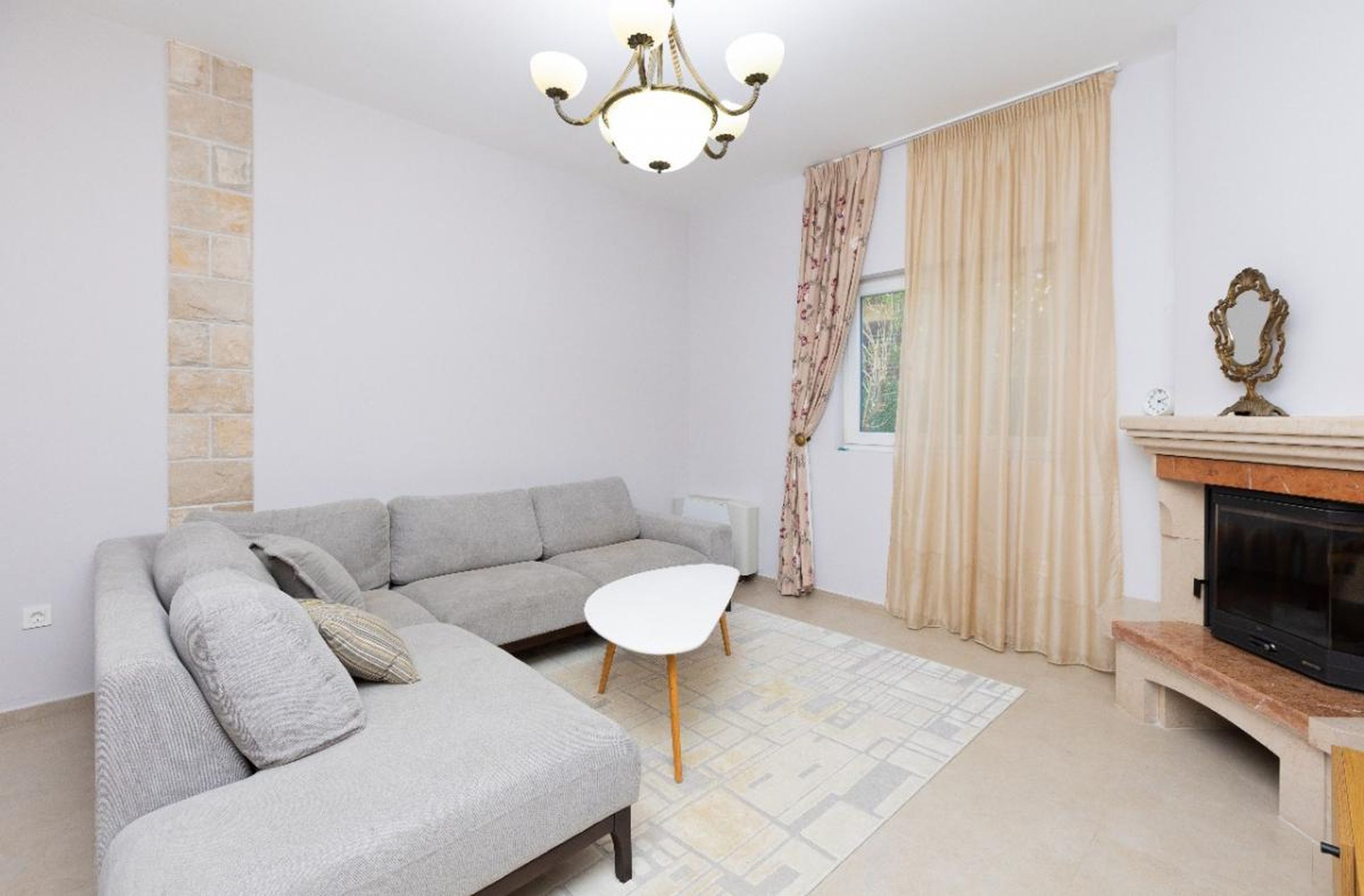 Living room in a house in Tivat, Montenegro: gray corner sofa, stone-clad fireplace, and a bright interior.