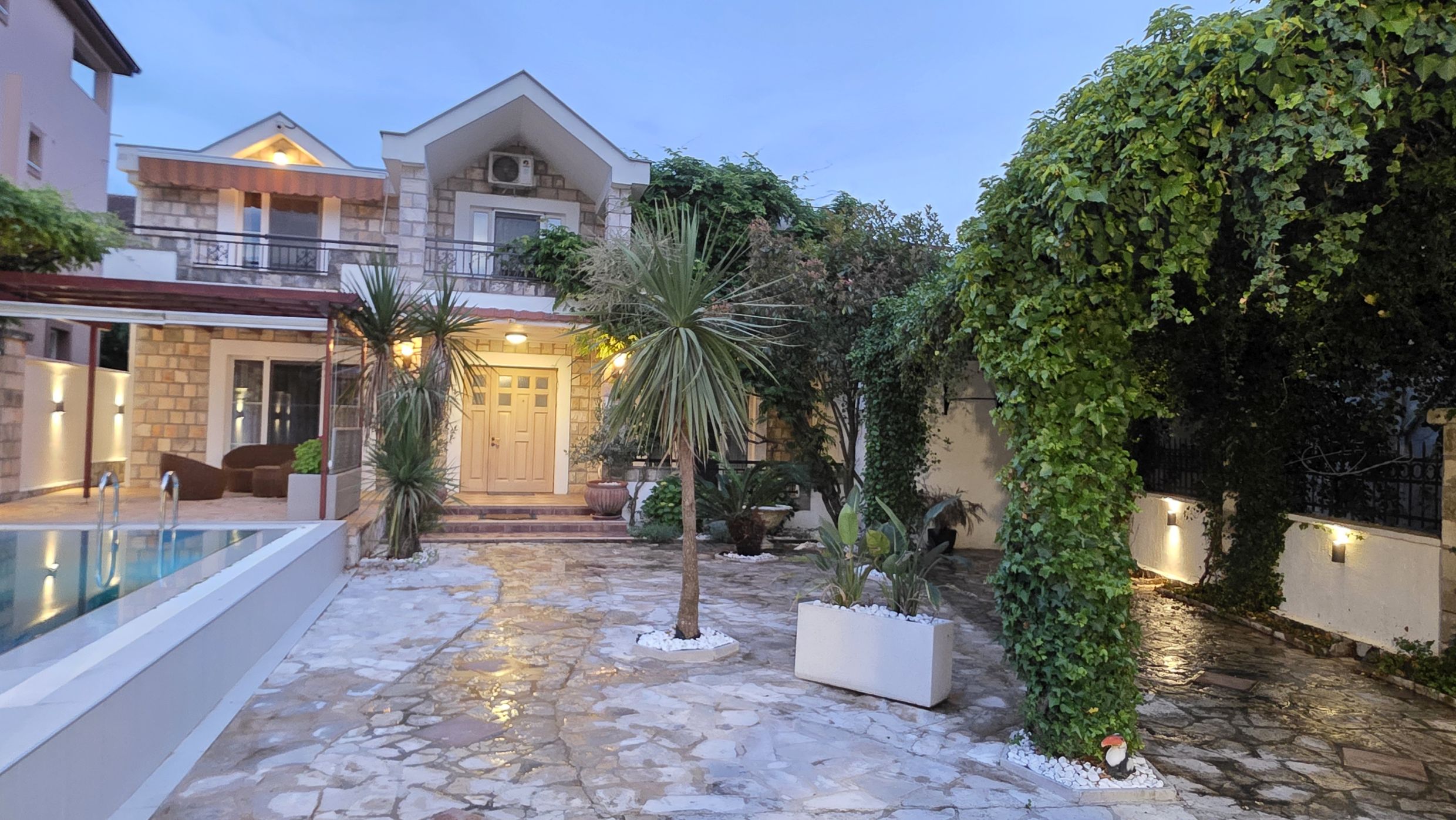 Two-story villa in Tivat, Montenegro: stone facade, swimming pool, well-kept garden with palm trees, and a cozy terrace.