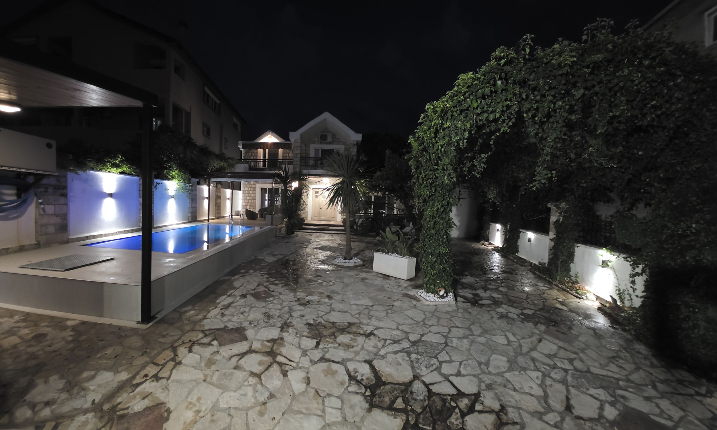 Two-story house in Tivat, Montenegro, with night lighting, a private pool, and a landscaped stone courtyard.