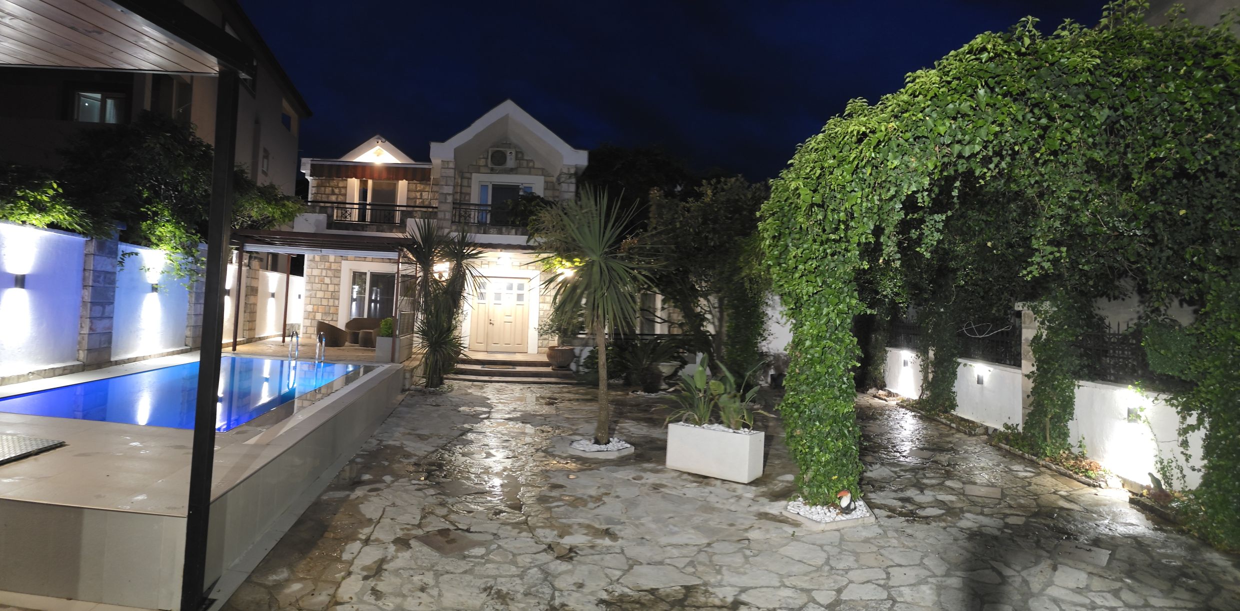 Two-story house in Tivat, Montenegro, with a swimming pool, stone terrace, landscaping, and evening lighting.