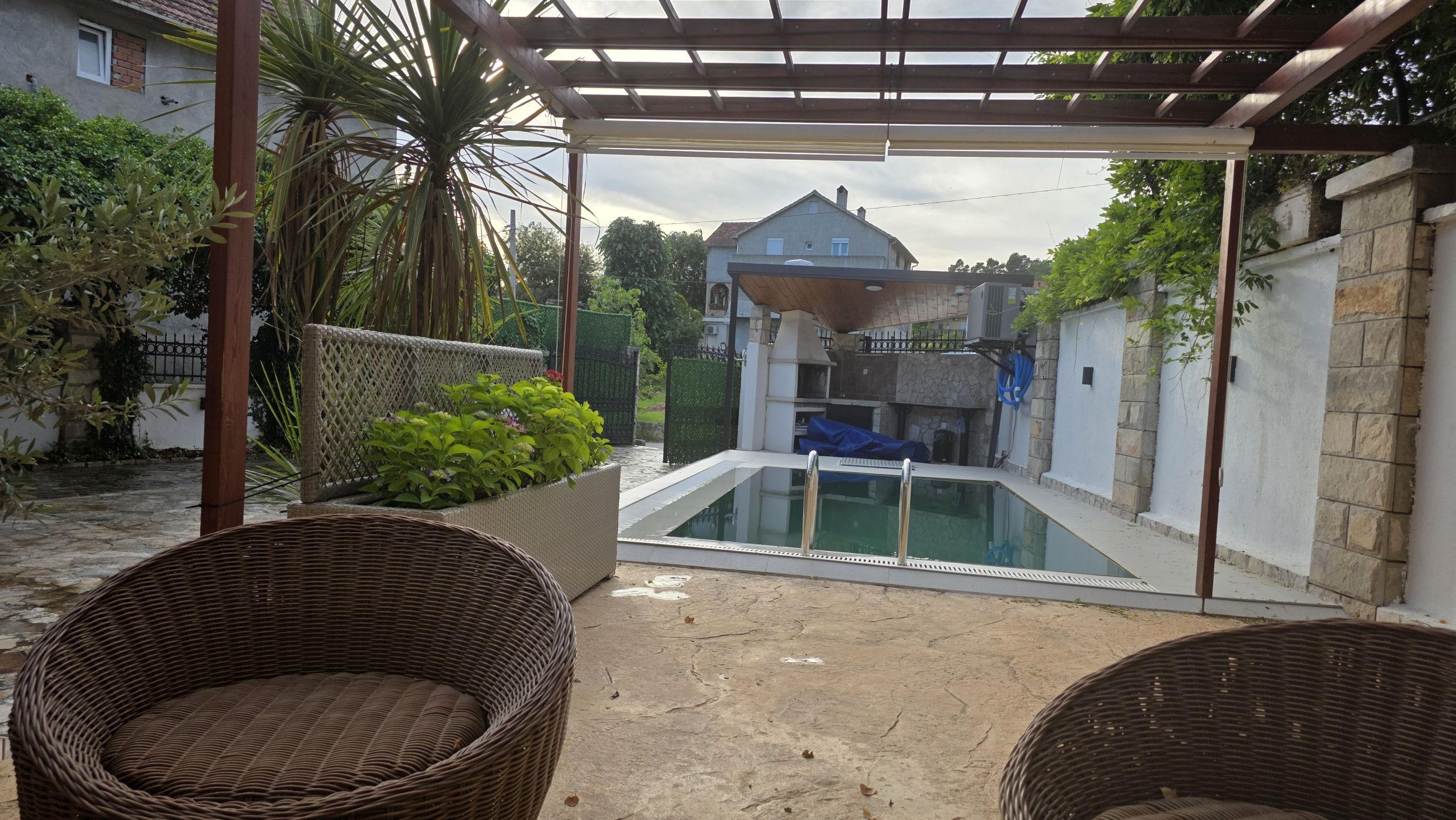 Terrace with a pool and barbecue area in a private house in Tivat, Montenegro: wicker furniture and a view of the garden.