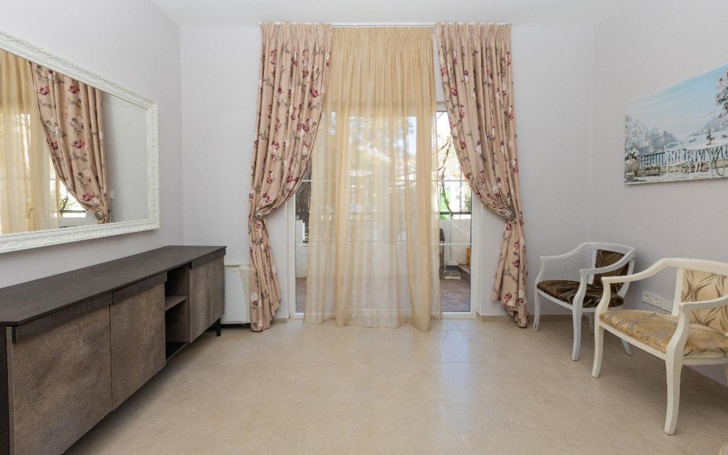 Bright living room in a house in Tivat, Montenegro: a mirror in a white frame, classic chairs, and access to the terrace.