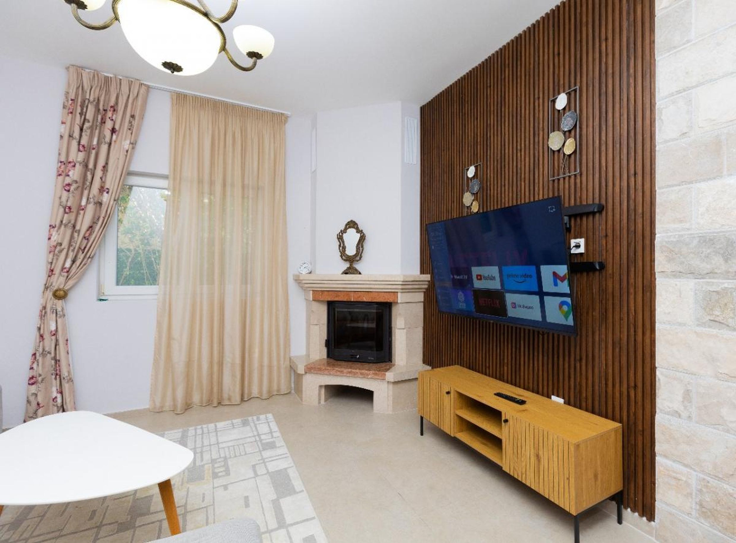 Living room in a house in Tivat, Montenegro: fireplace, TV area with wooden slats, modern furniture, and a cozy interior.
