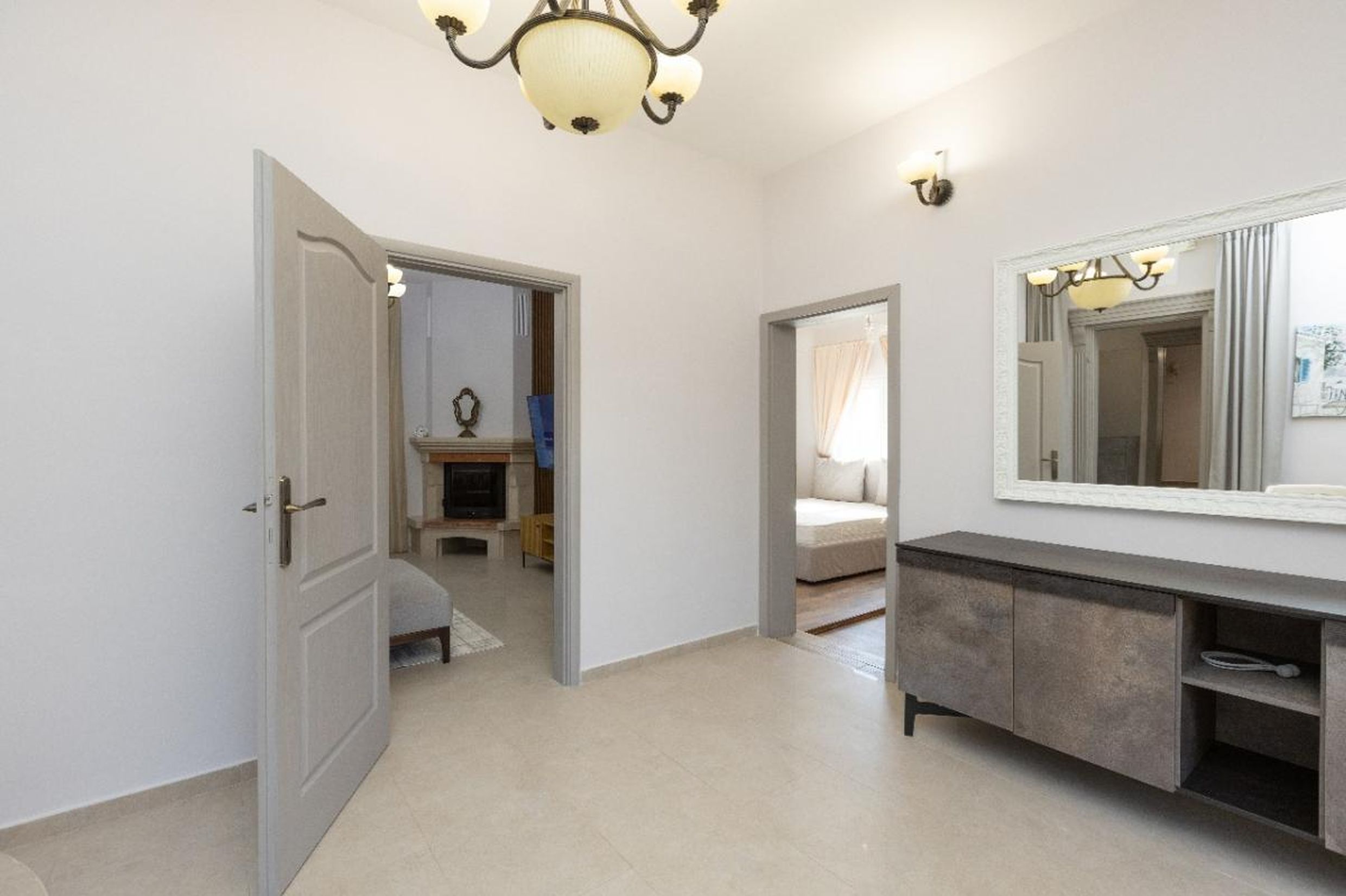 Bright hallway with a dresser and mirror in a house in Tivat, Montenegro, view of the living room with a fireplace and the bedroom.
